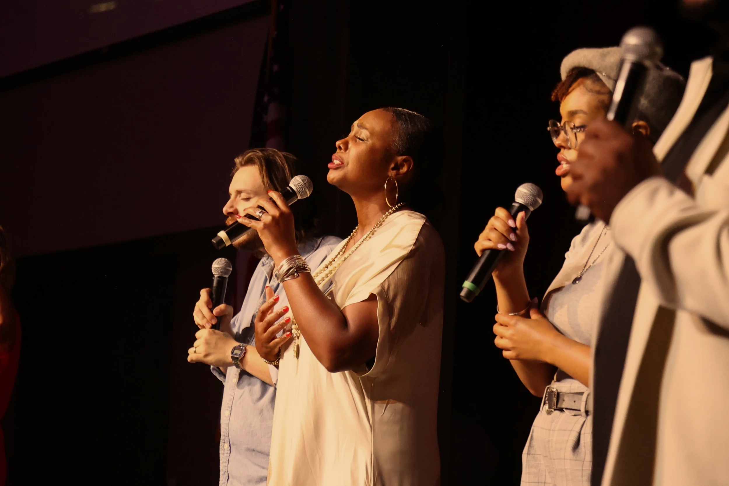 one young men and two women singing with their eyes closed on a stage leading worship