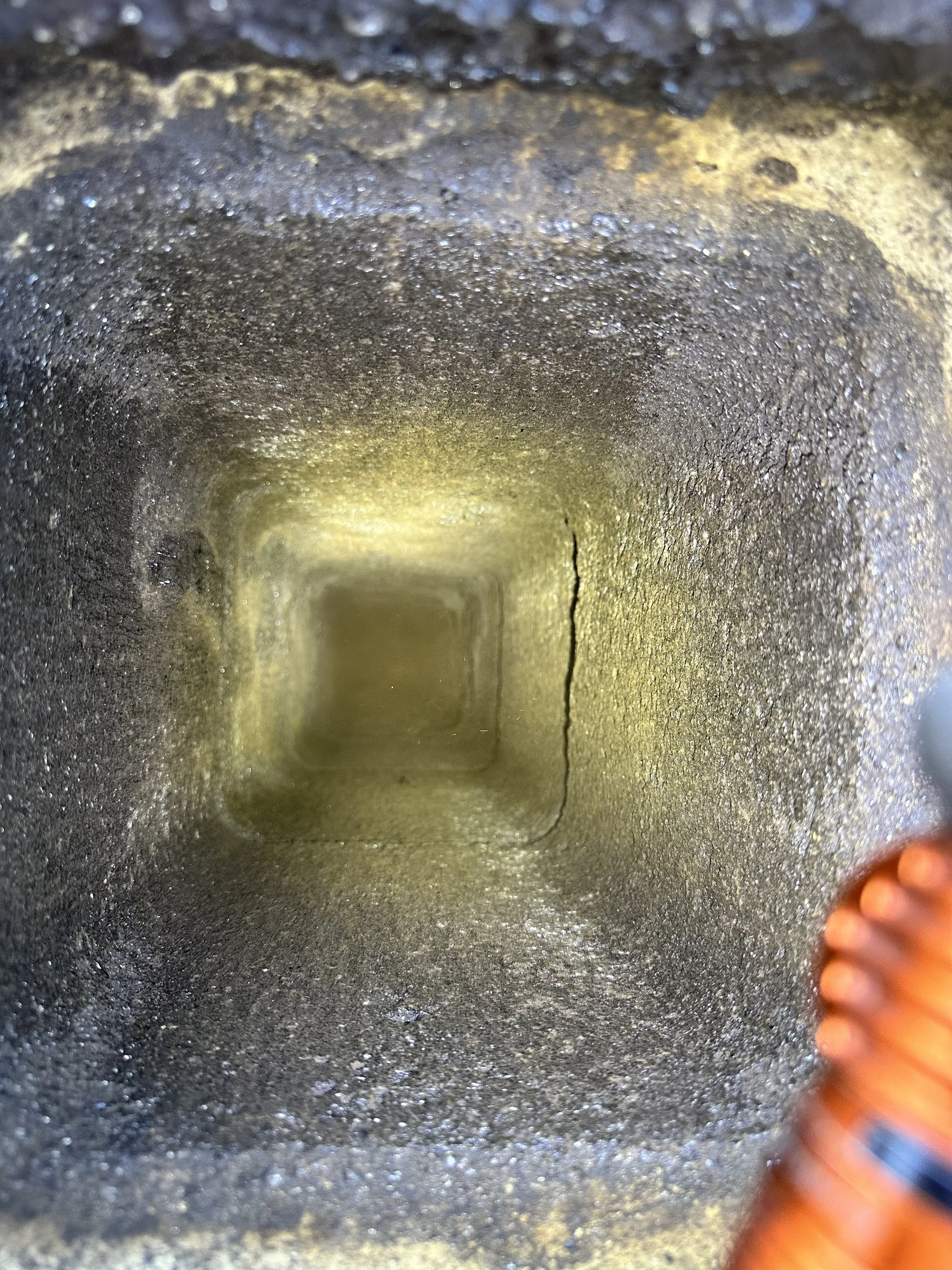 Vue en profondeur d'un cylindre ou trou avec une surface sombre et rugueuse en métal, éclairée de manière diffuse, avec un objet orange partiel visible sur le côté droit.
