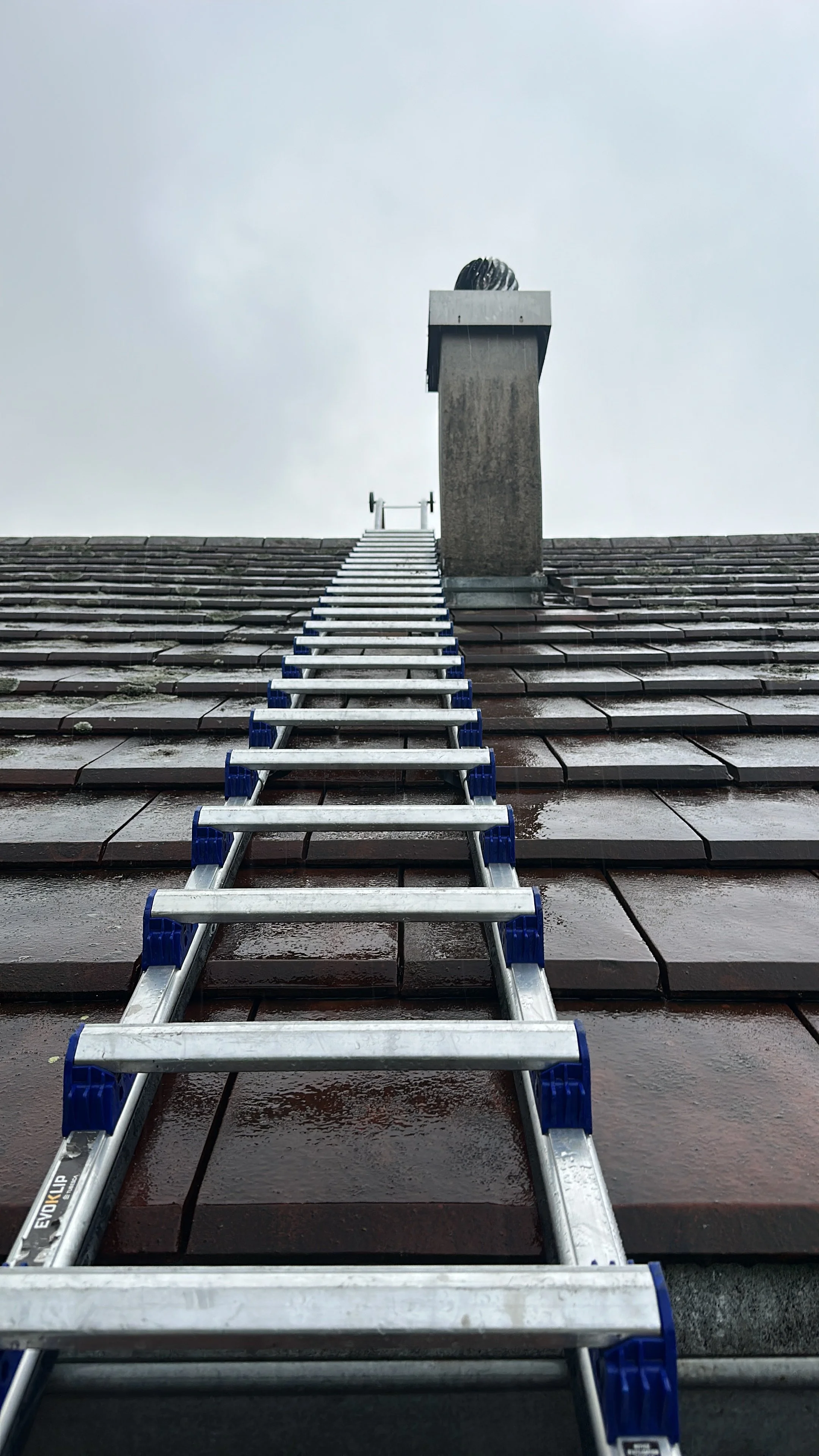 Ladder sur un toit en tuiles humides menant à une cheminée.