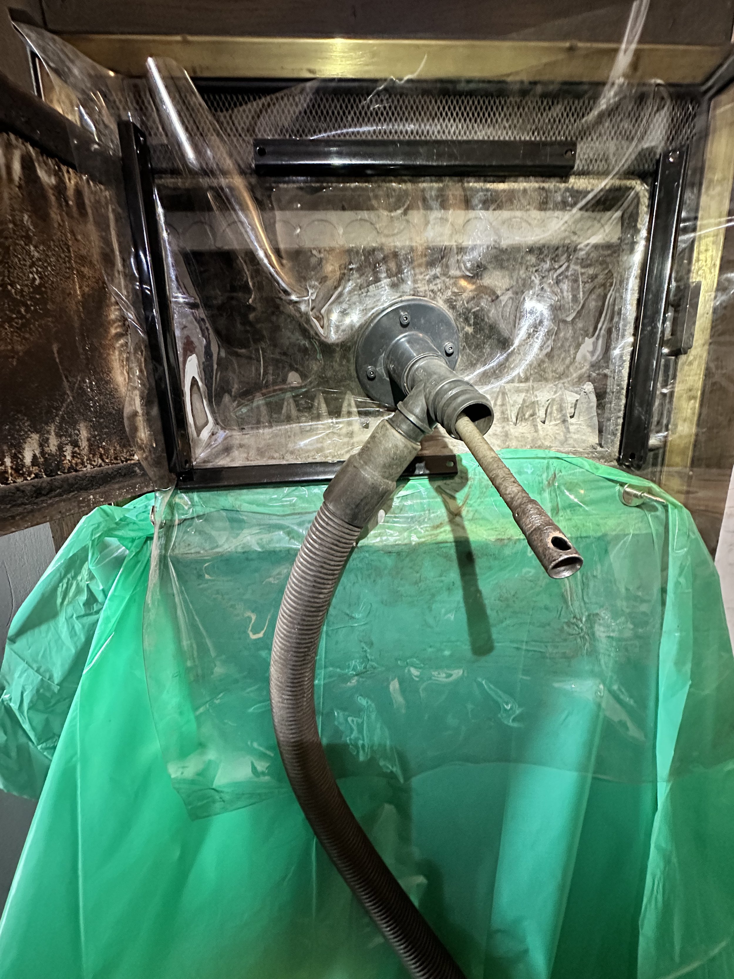 Une cabine de nettoyage à vapeur ou à haute pression, avec un tuyau flexible, une surface métallique et une protection en plastique vert, utilisée pour le nettoyage industriel.
