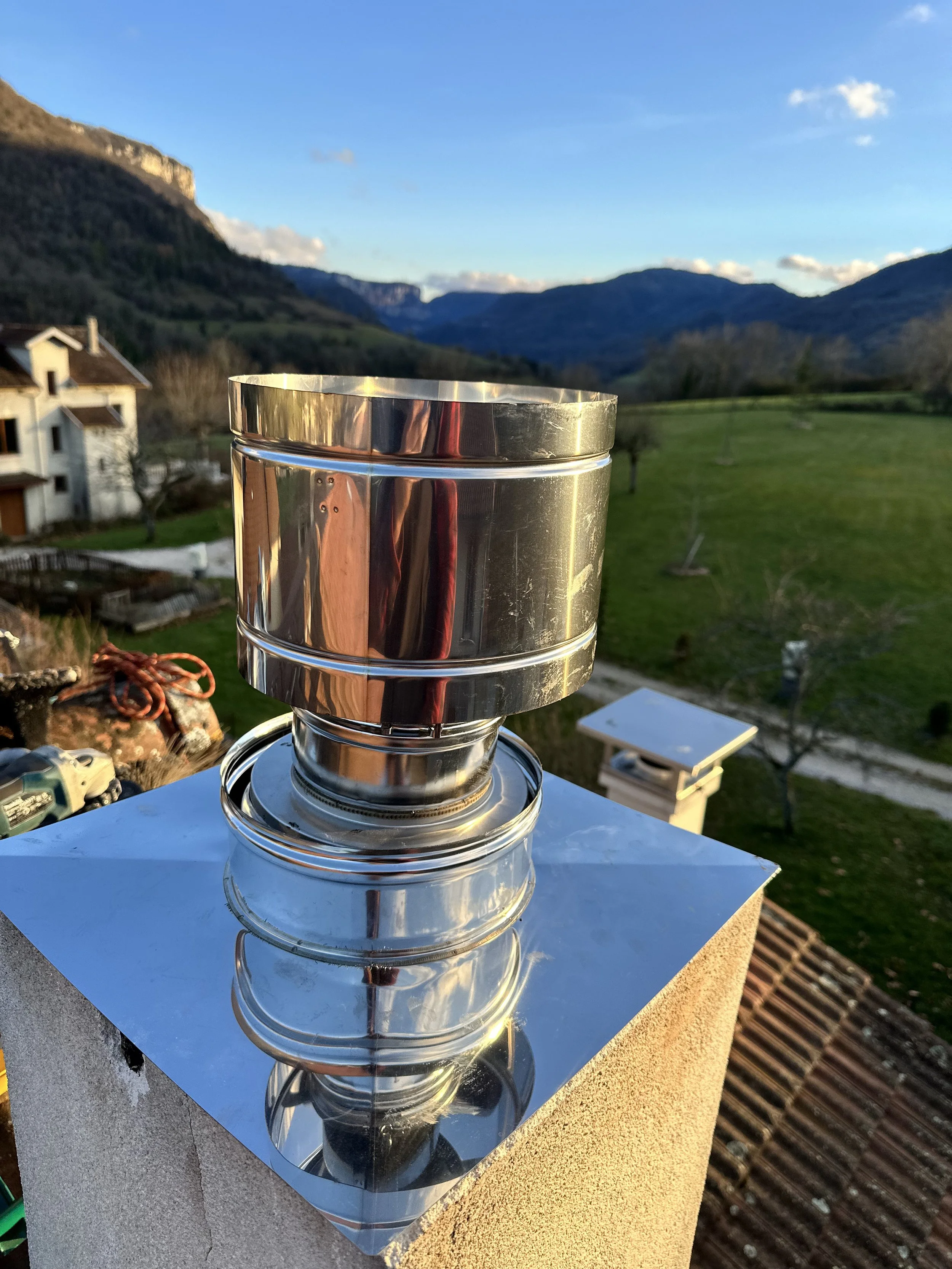 Un four à pizza en acier inoxydable posé sur une surface avec un paysage de montagnes et un ciel bleu en arrière-plan.