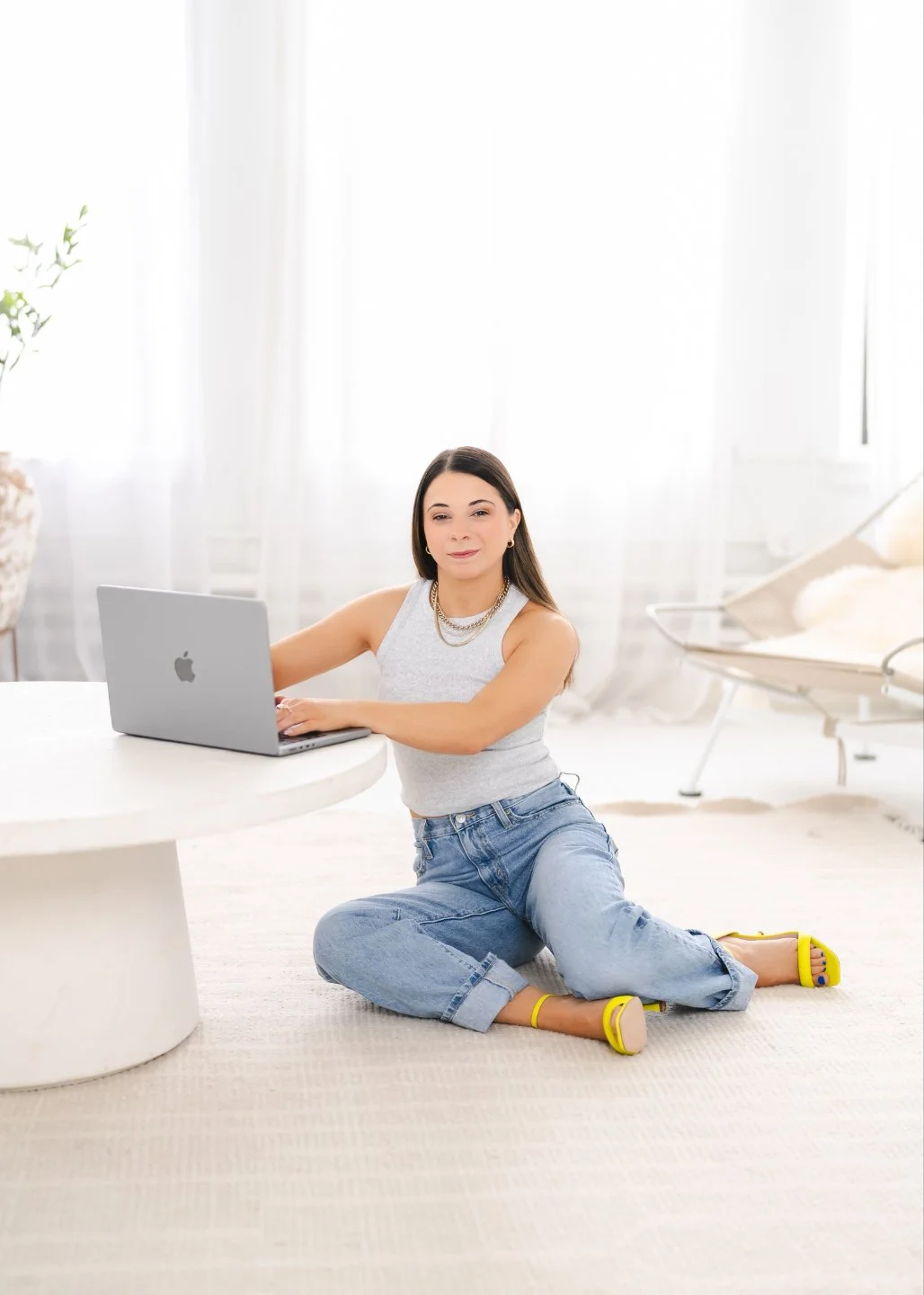 Woman sitting on the floor in a bright room using a laptop at a white round table.