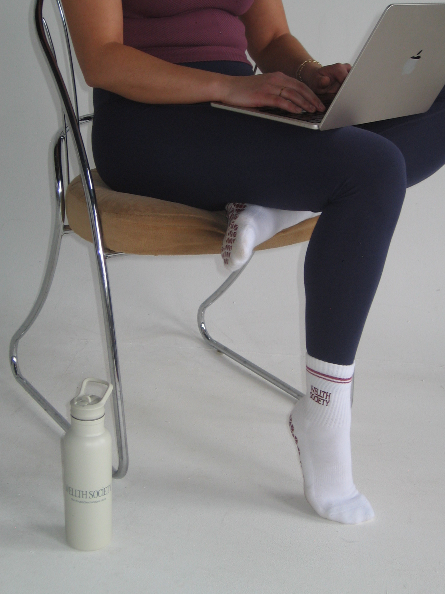 Person sitting on a chair with a laptop on their lap, wearing dark pants, a short-sleeved top, and white socks with lettering.