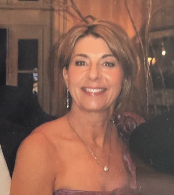 Image of Ellen Catapang, of Infusion Insurance, wearing earrings and a necklace, dressed in a purple outfit, in a warmly lit indoor setting.