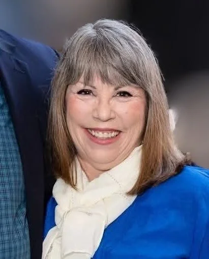 Image of Deb Crispo, of Infusion Insurance, standing on a beach during sunset, holding a drink, wearing a bright red top and a colorful scarf.