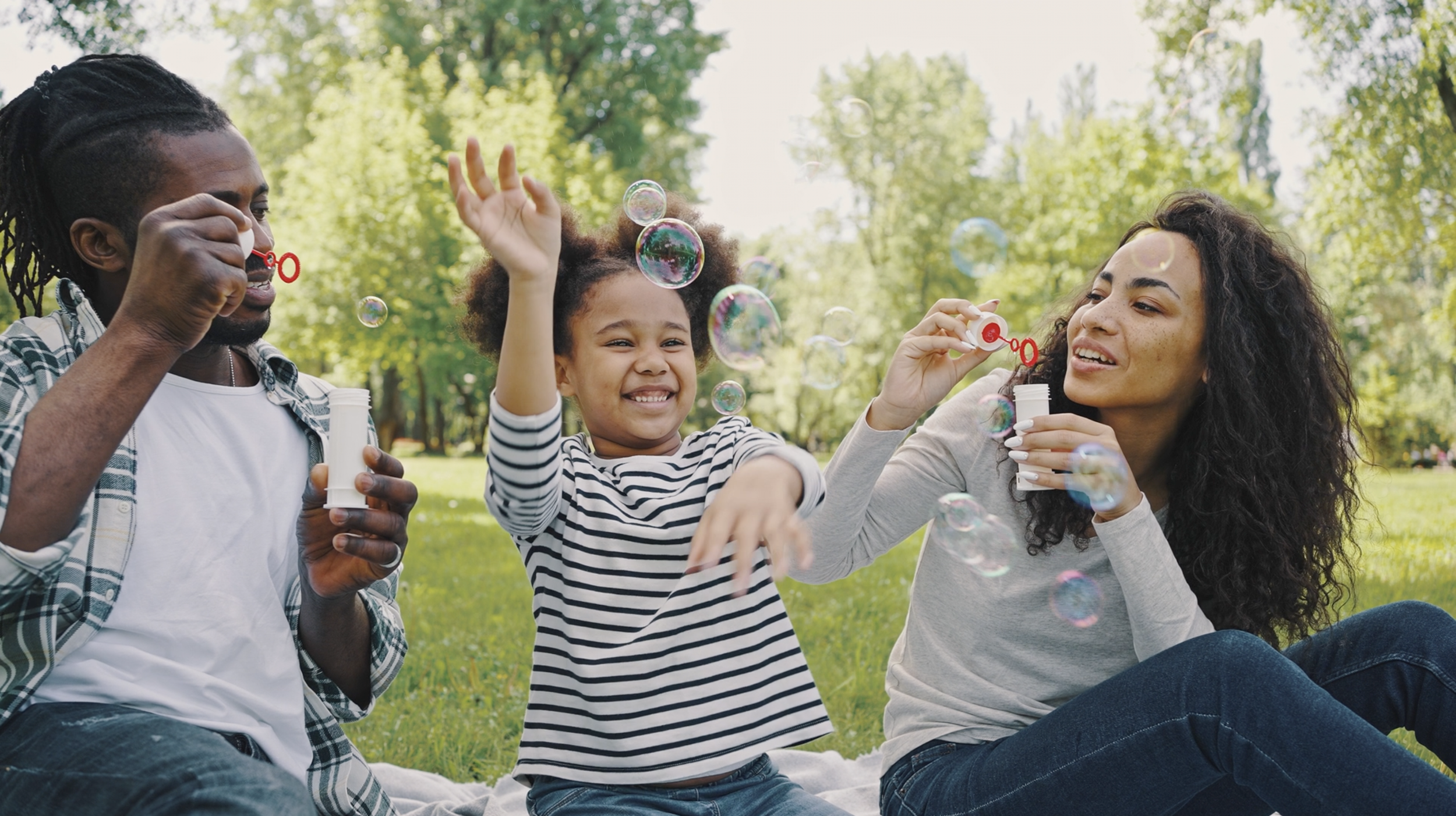 Une famille de trois personnes, deux adultes et un enfant, en train de jouer à souffler des bulles, à développer la communication et à s'amuser à connecter ensemble sur le Rive-Sud de Montréal