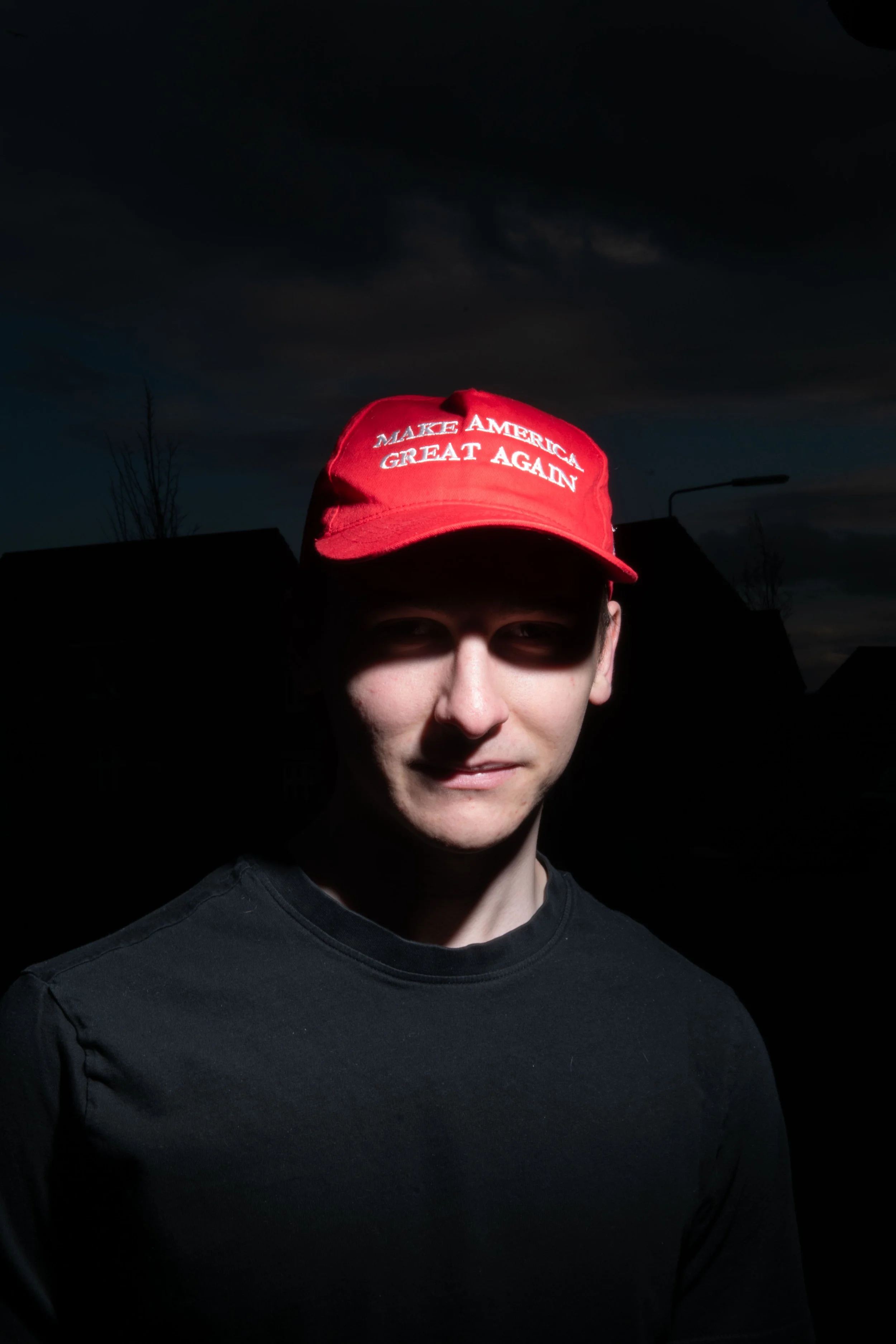 A person wearing a red 'Make America Great Again' baseball cap and a black shirt, with a dark cloudy sky in the background.