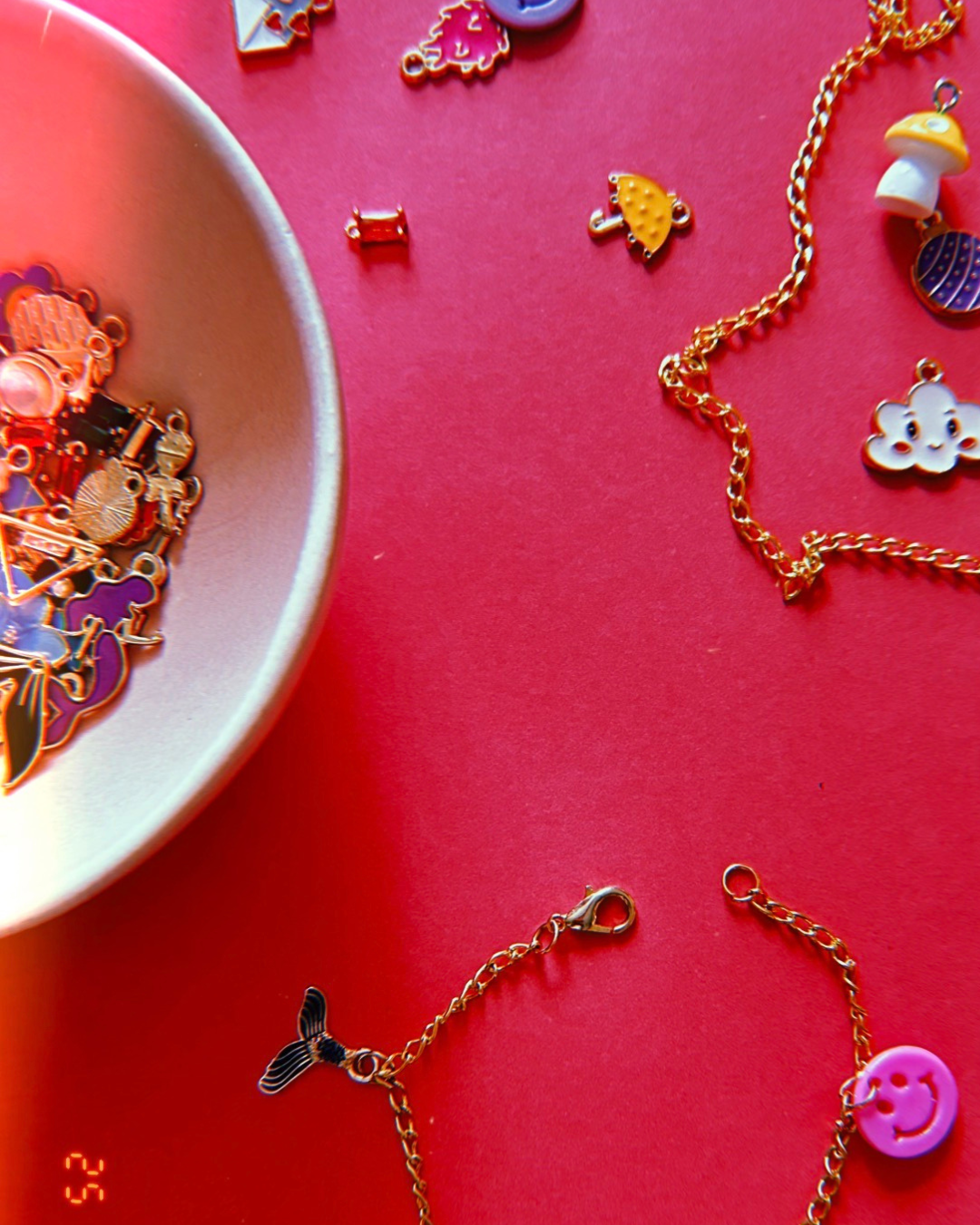 Colorful necklaces with various charms, some are in a small white dish and others are scattered on a red surface.