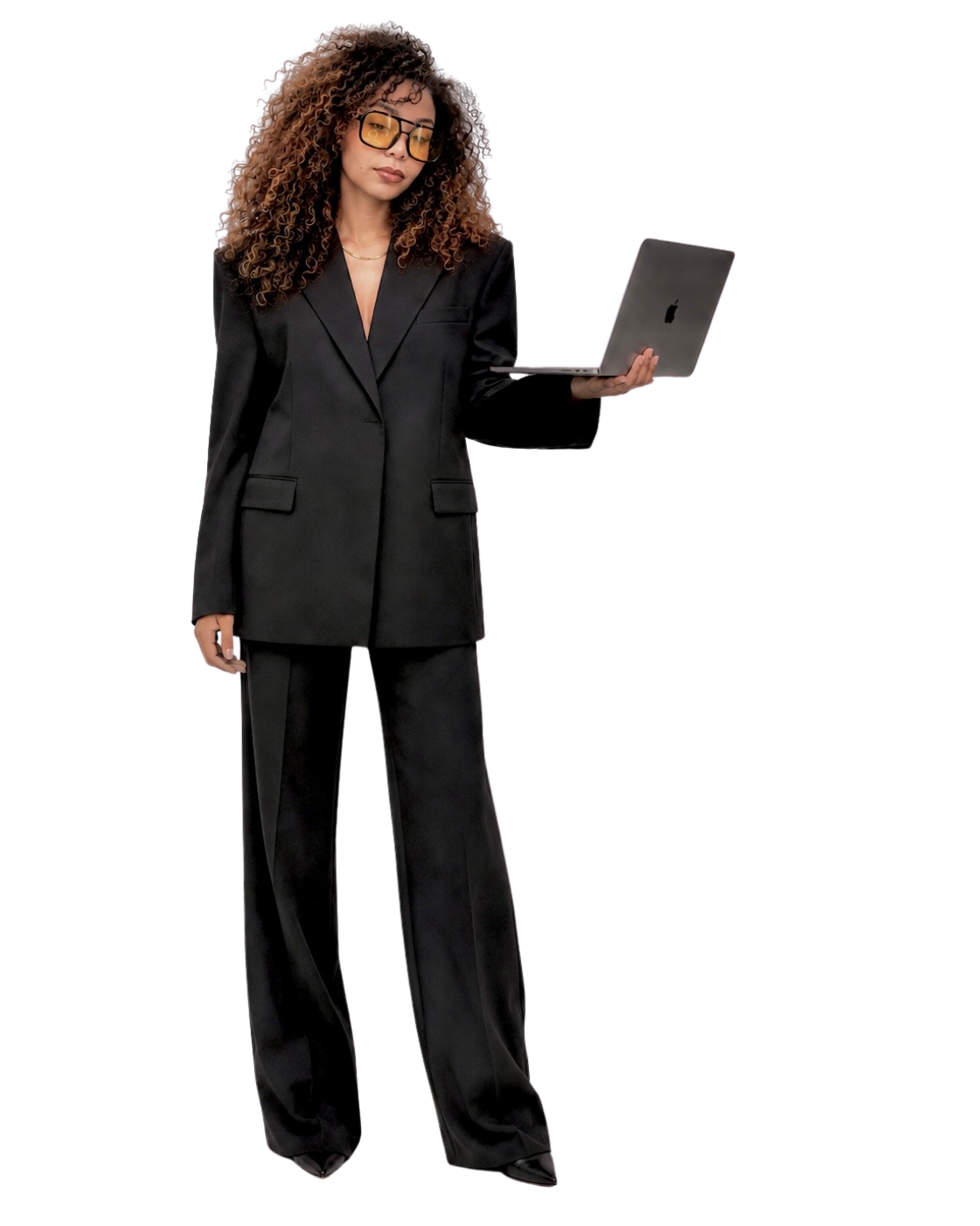 Une femme en costume noir, avec des lunettes jaunes, tient un ordinateur portable dans sa main, en position debout.
