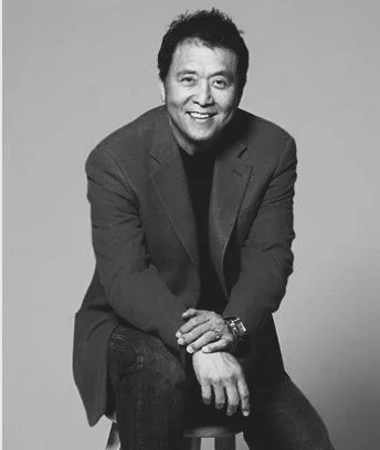 Homme souriant, en costume gris, assis sur une chaise, photo en noir et blanc.