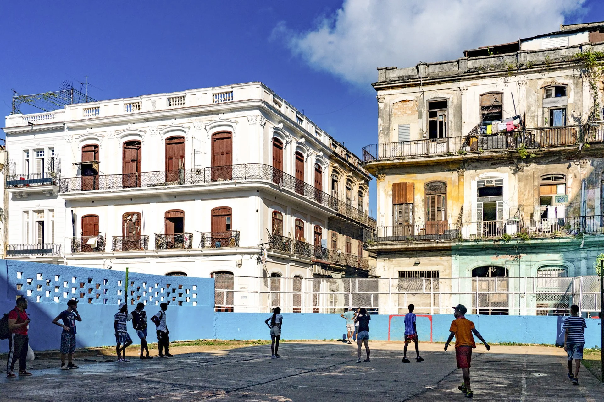 A group of children playing soccer on a school yard with old, colorful buildings in the background.