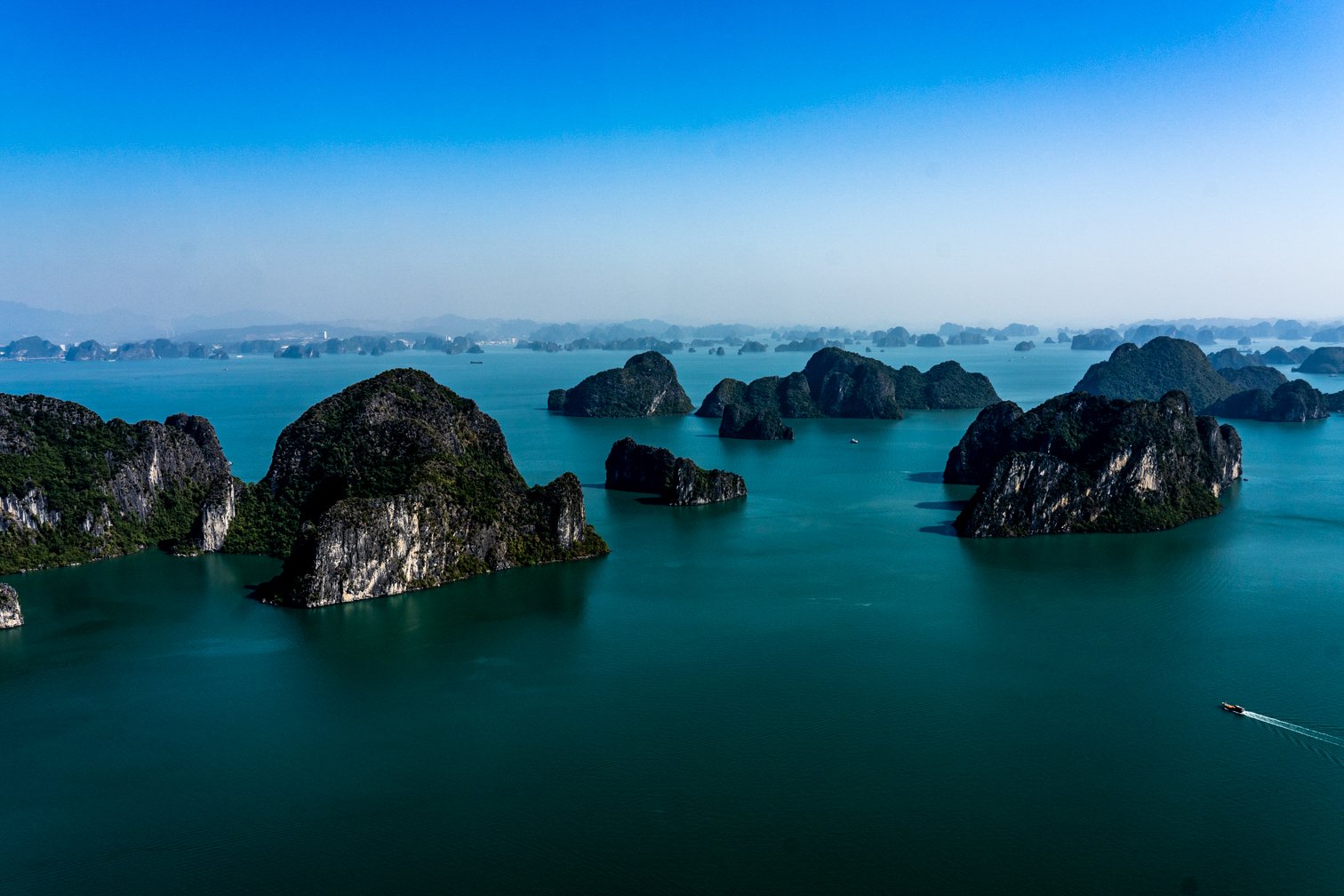 Scenic view of numerous limestone islands and islets in emerald green waters, with a small boat leaving a trail behind.