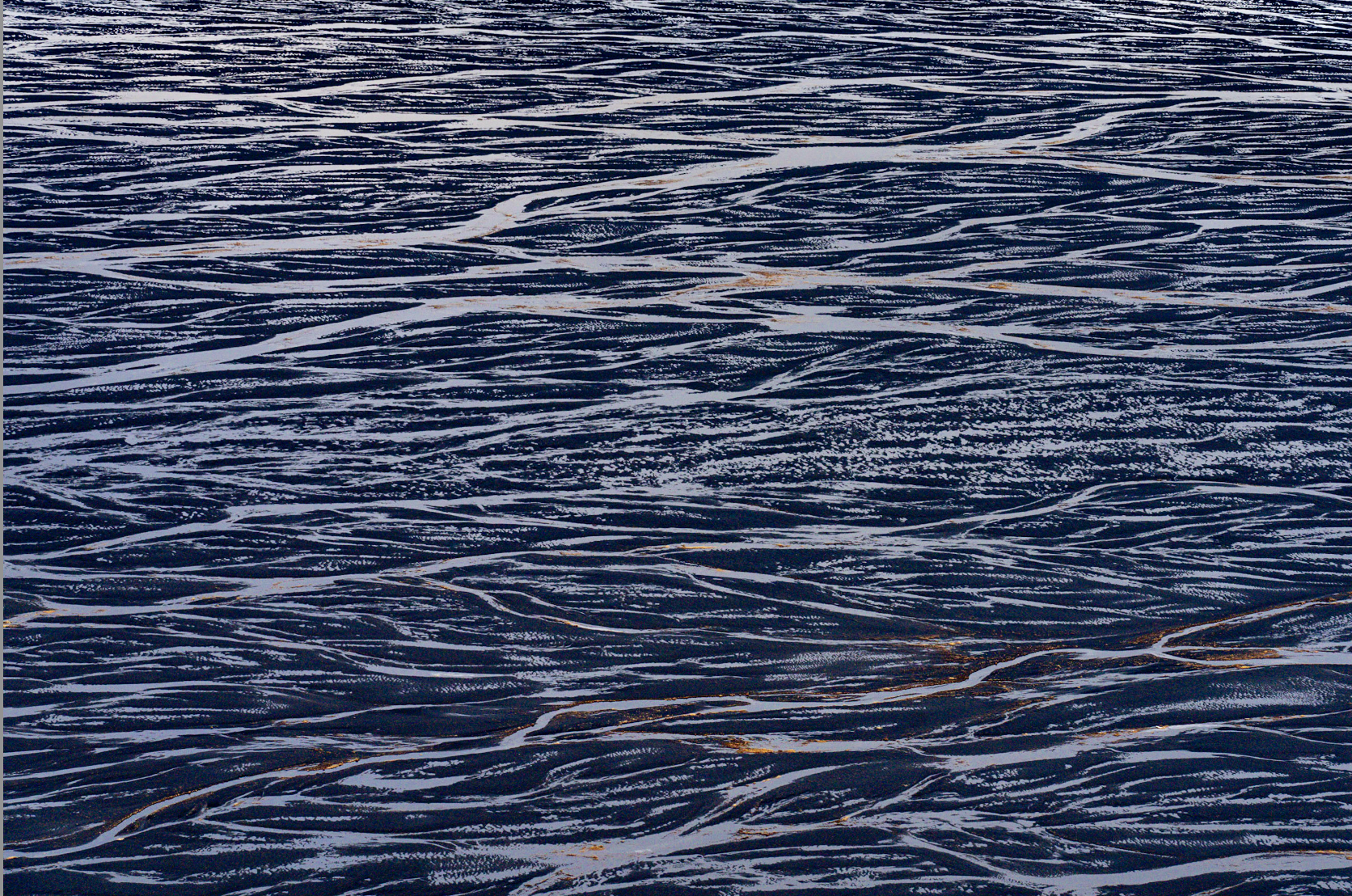 Close-up of a body of water with numerous dark, elongated, and wavy ripples on the surface.