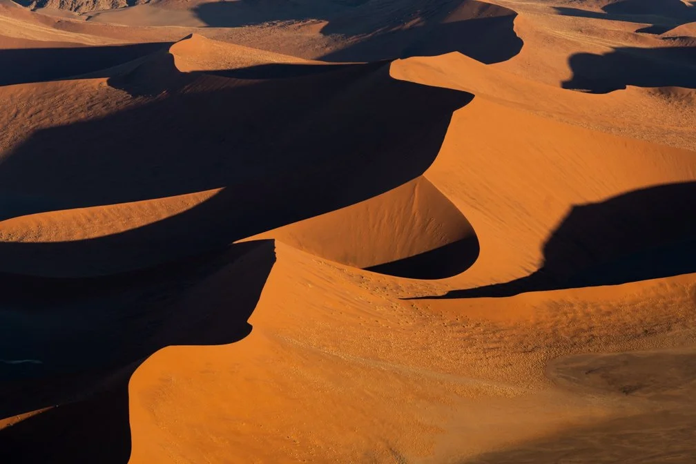 Sand dunes in a desert landscape with shadows and warm lighting.