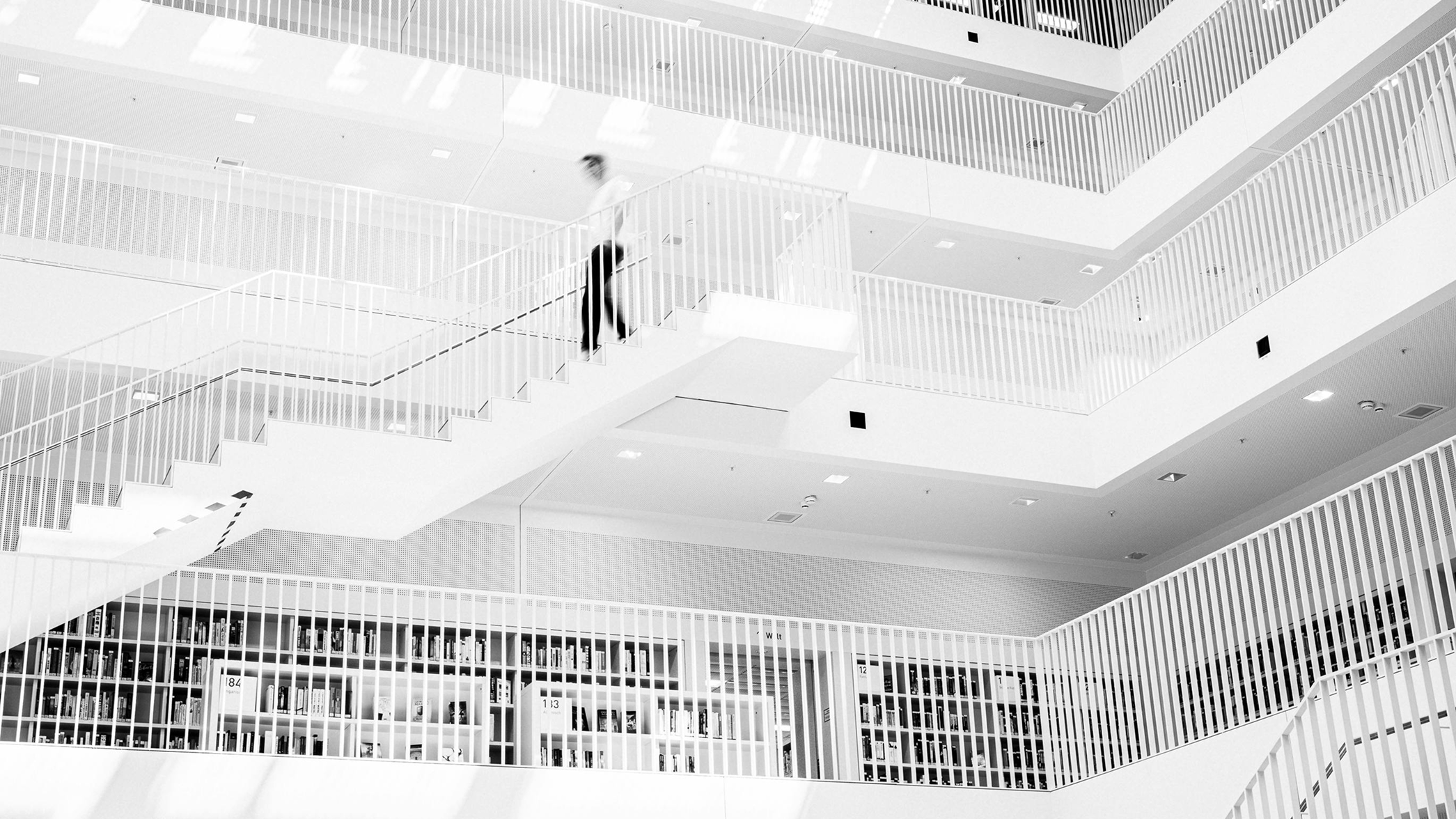 Black and white photo of a man walking down stairs in a modern library