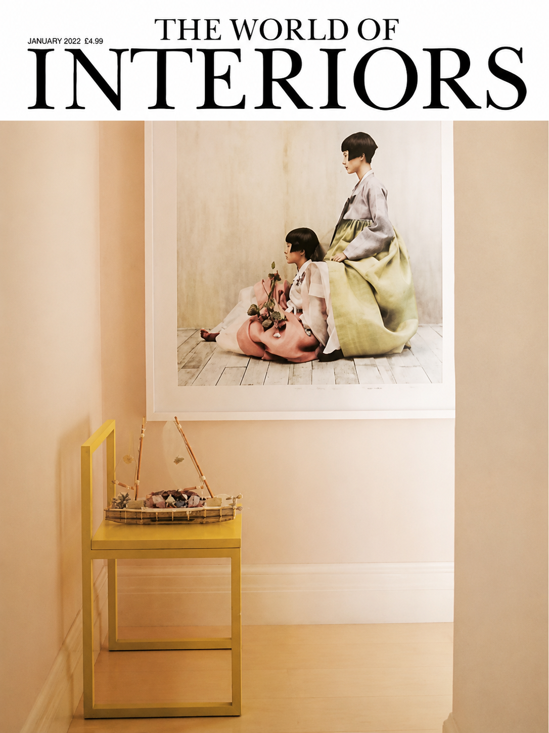 An interior space with a yellow chair holding a small basket filled with pink, purple, and green decorative items, set against beige walls. A large framed photo of two women in traditional Korean hanbok dresses is hung on the wall.