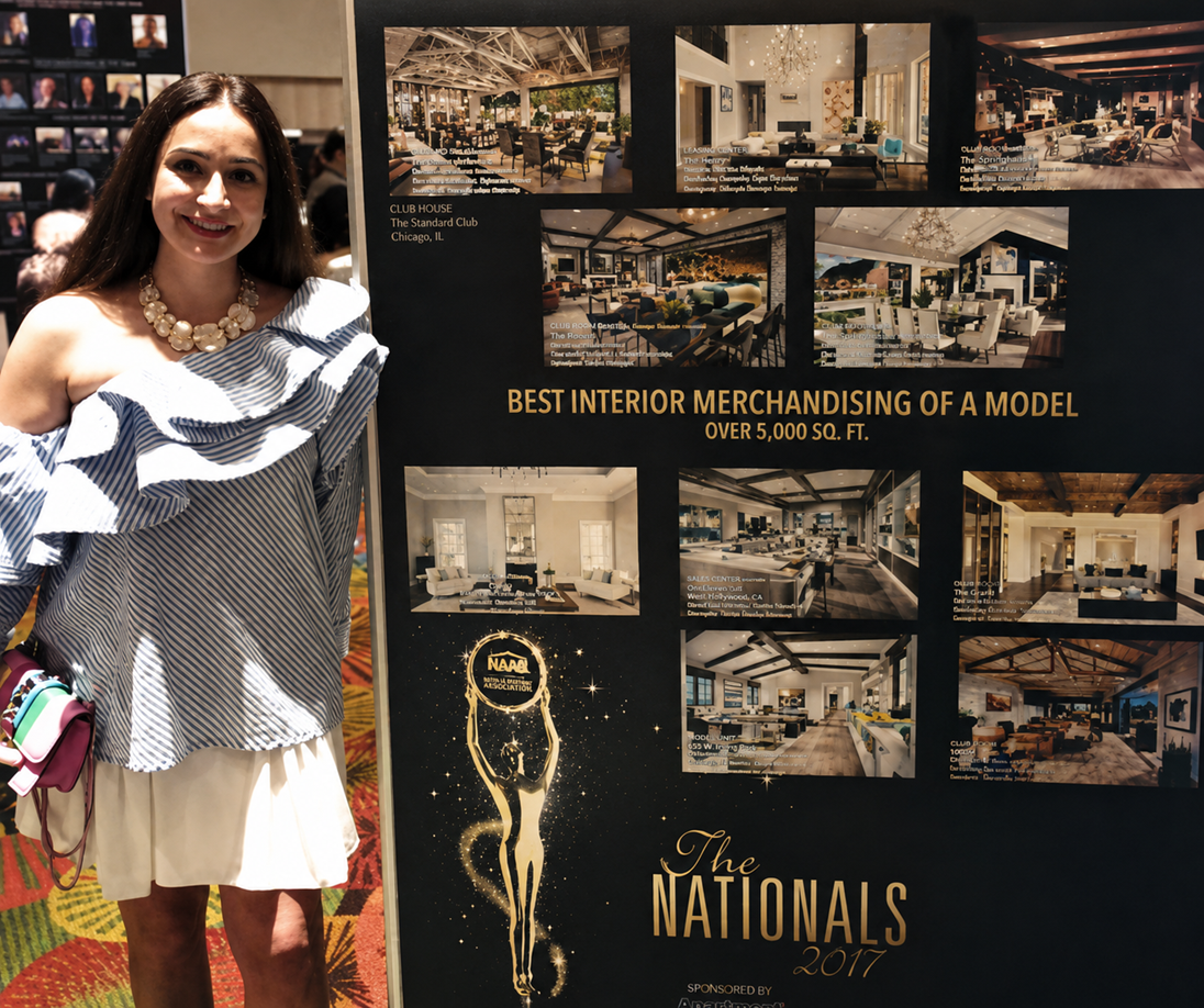 A woman smiling and standing next to an interior design display board at a trade show or exhibition, featuring images and information about interior merchandising services.