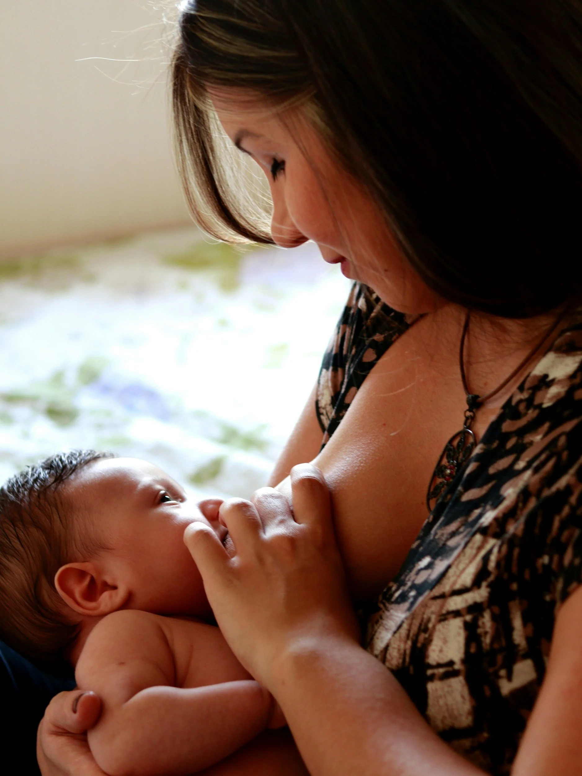 Close-up of a woman breastfeeding a baby outdoors, with both lying on a blanket.