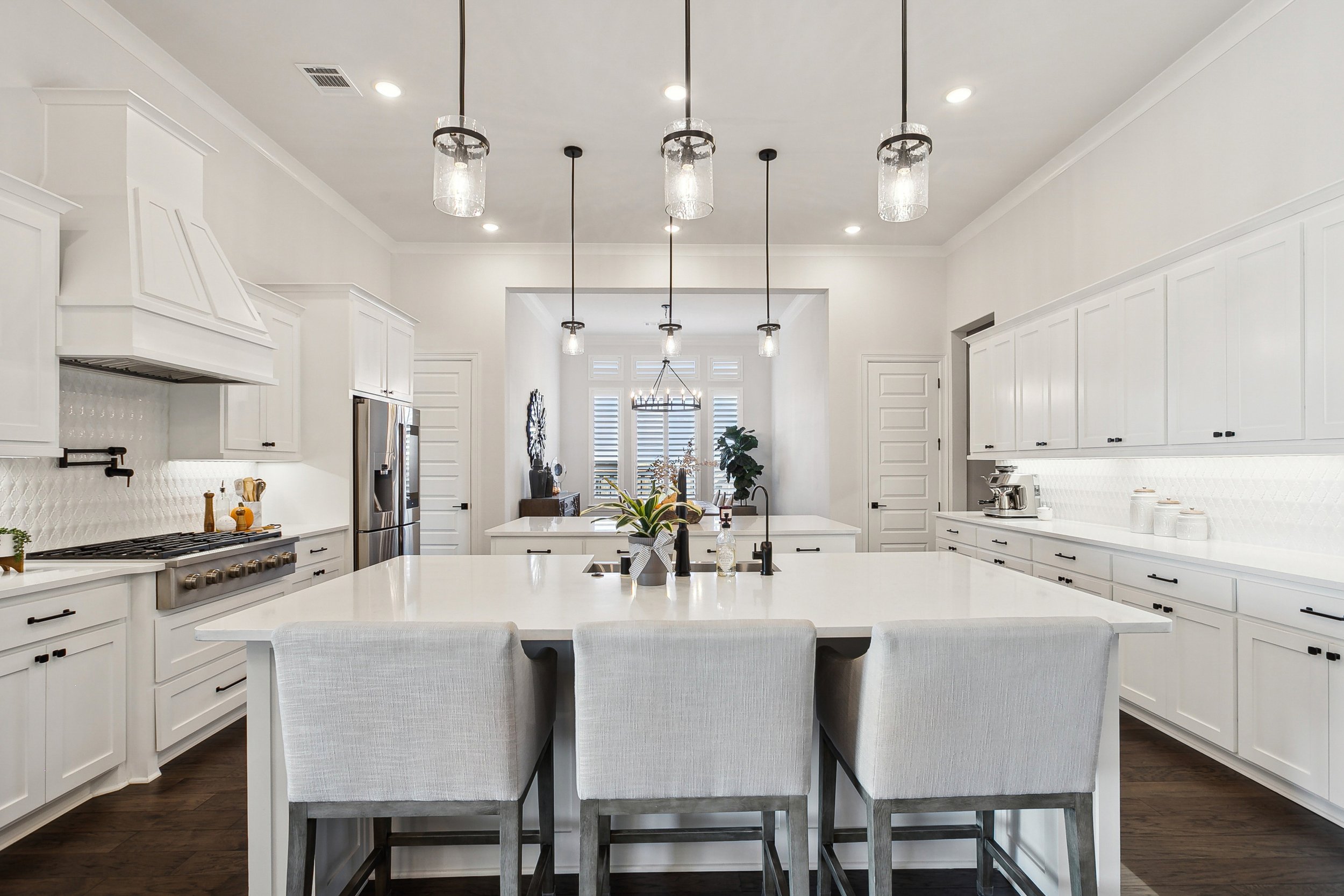 Modern white kitchen with island, pendant lights, and dining area in the background.