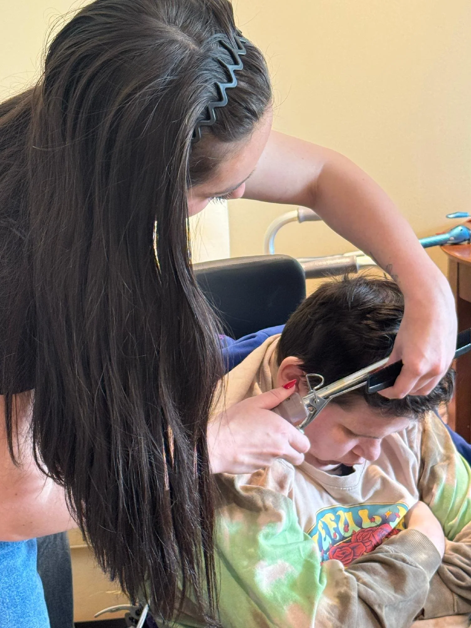 A woman with long dark hair, wearing a hair clip, is assisting a young boy with a medical hand brace or splint, helping him with his arm or hand.