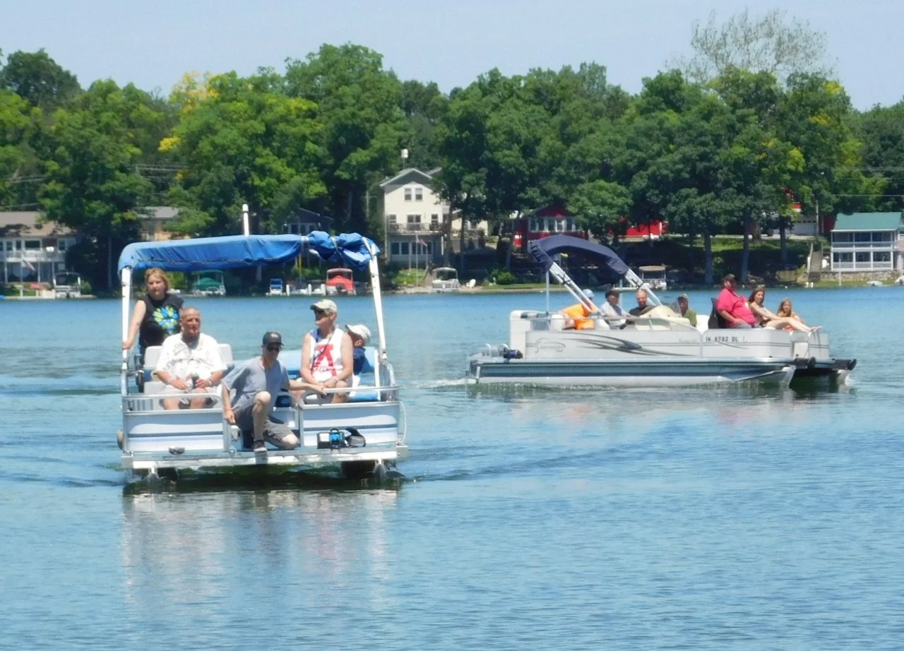 People boating on a lake with houses and trees in the background.