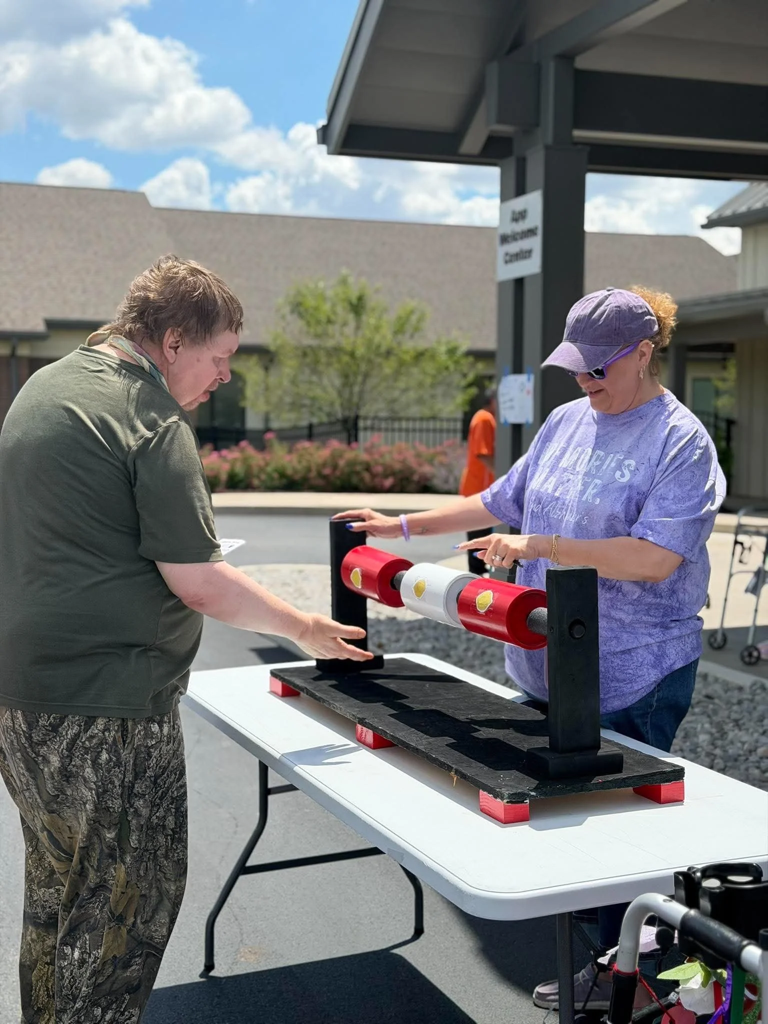 A man and a woman playing a game with a roulette wheel set up on a table outdoors on a sunny day.
