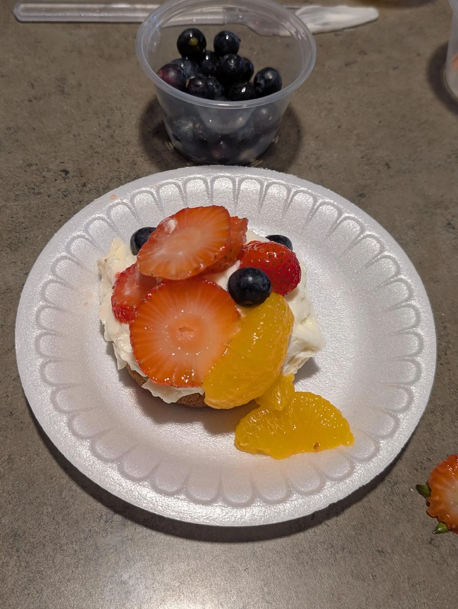 Dessert with sliced strawberries, blueberries, and canned peaches on a white paper plate.