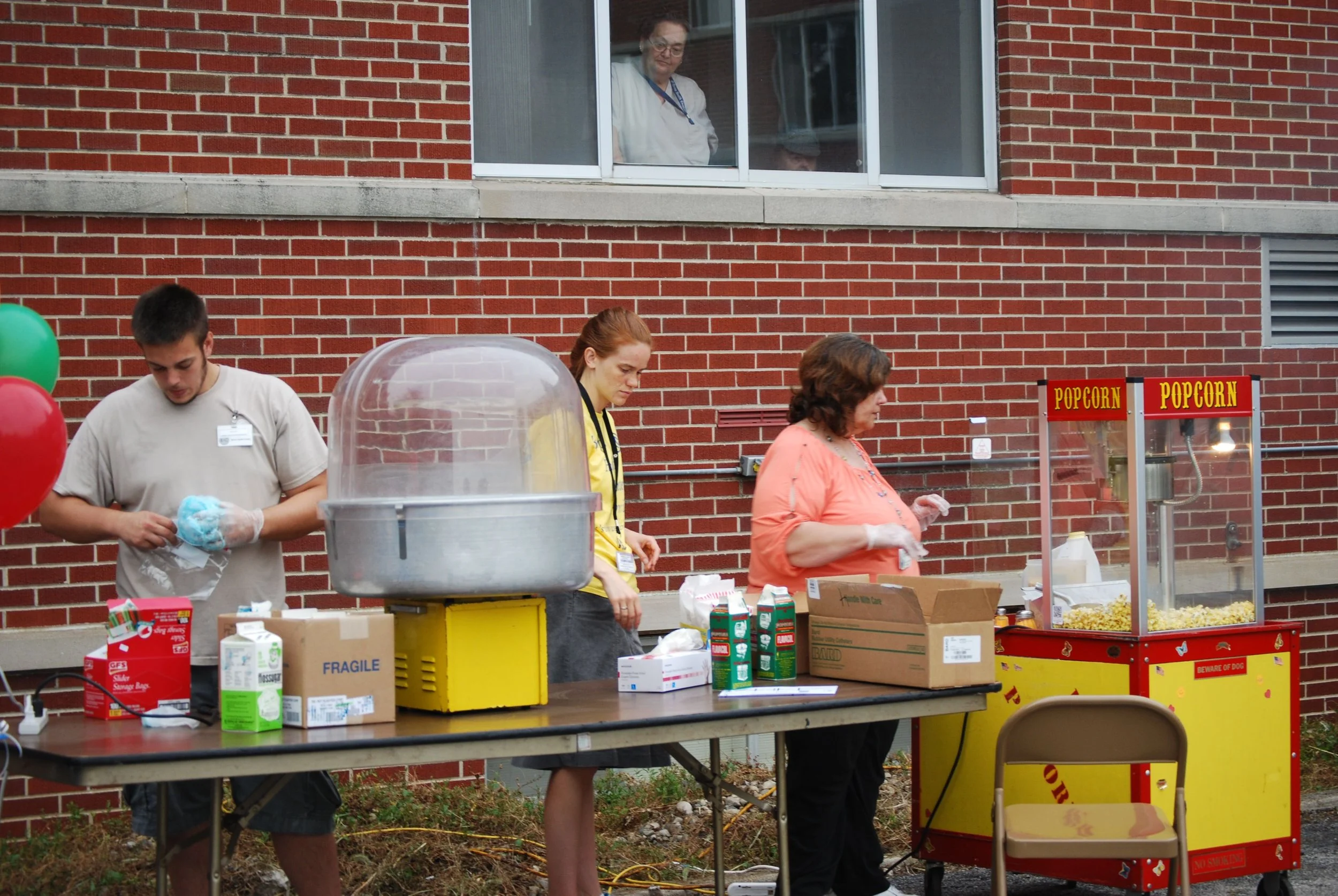 People serving popcorn and snacks at an outdoor event with a brick building in the background.