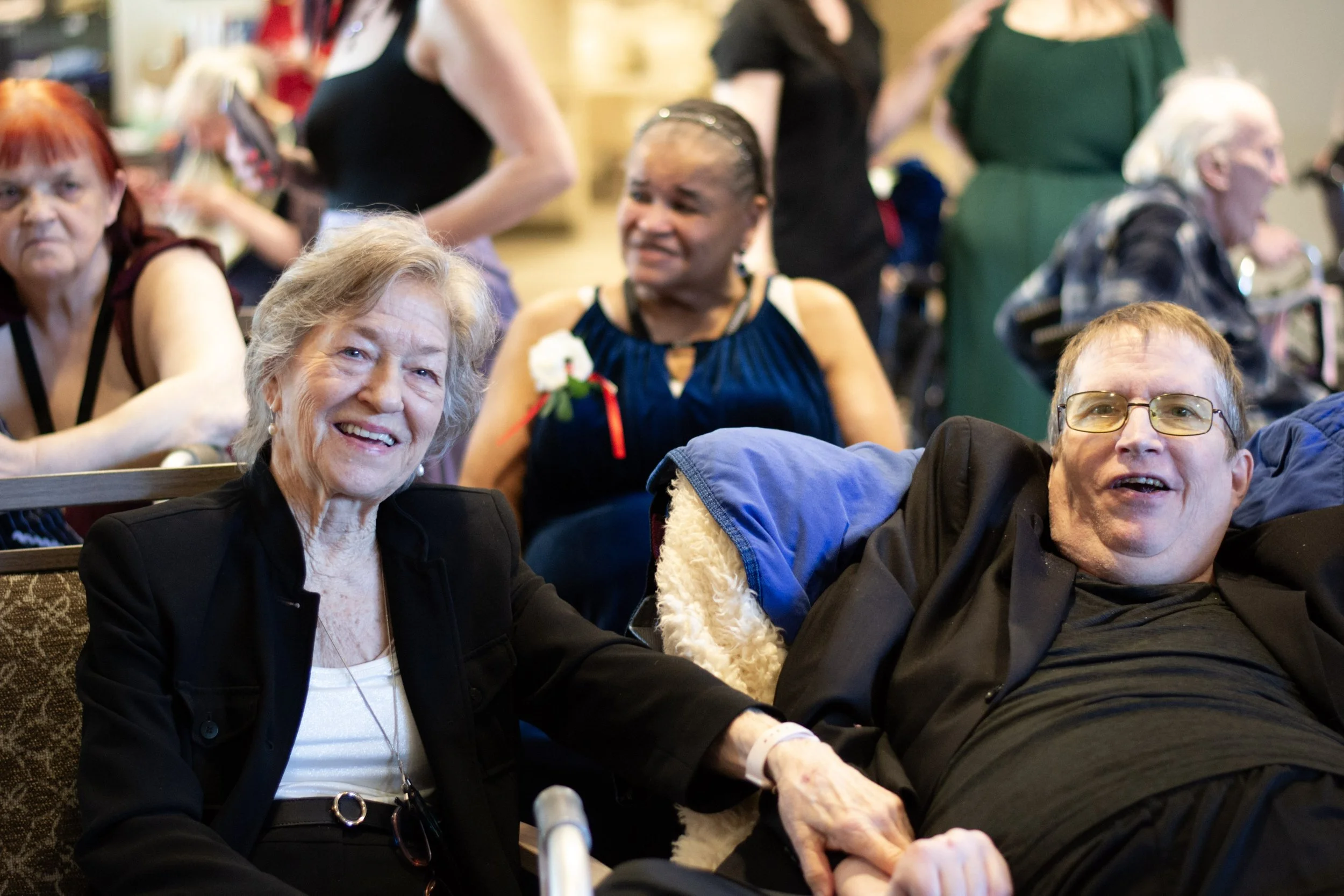 Group of elderly and middle-aged people gathered together, smiling and enjoying each other's company at an indoor event.