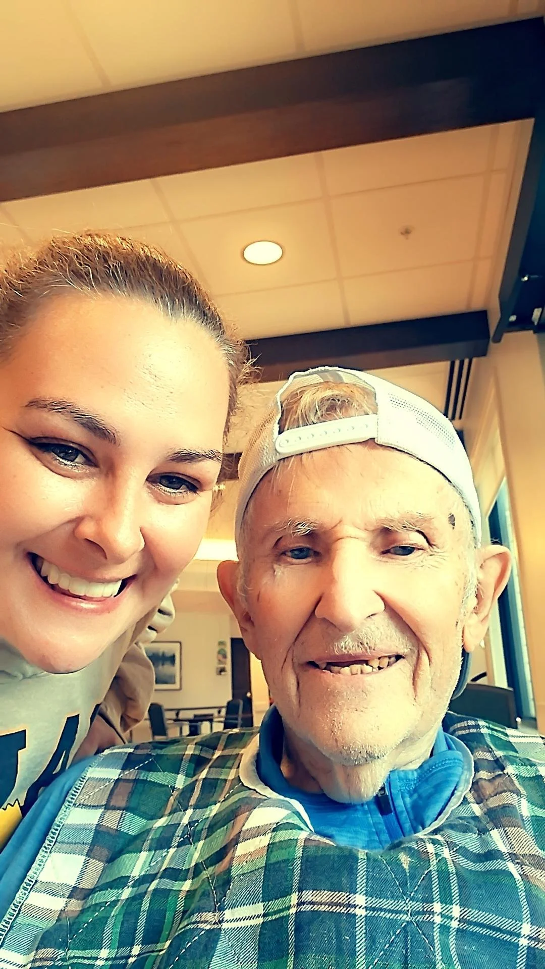 A young woman and an elderly man smiling for a selfie inside a cafe or restaurant.