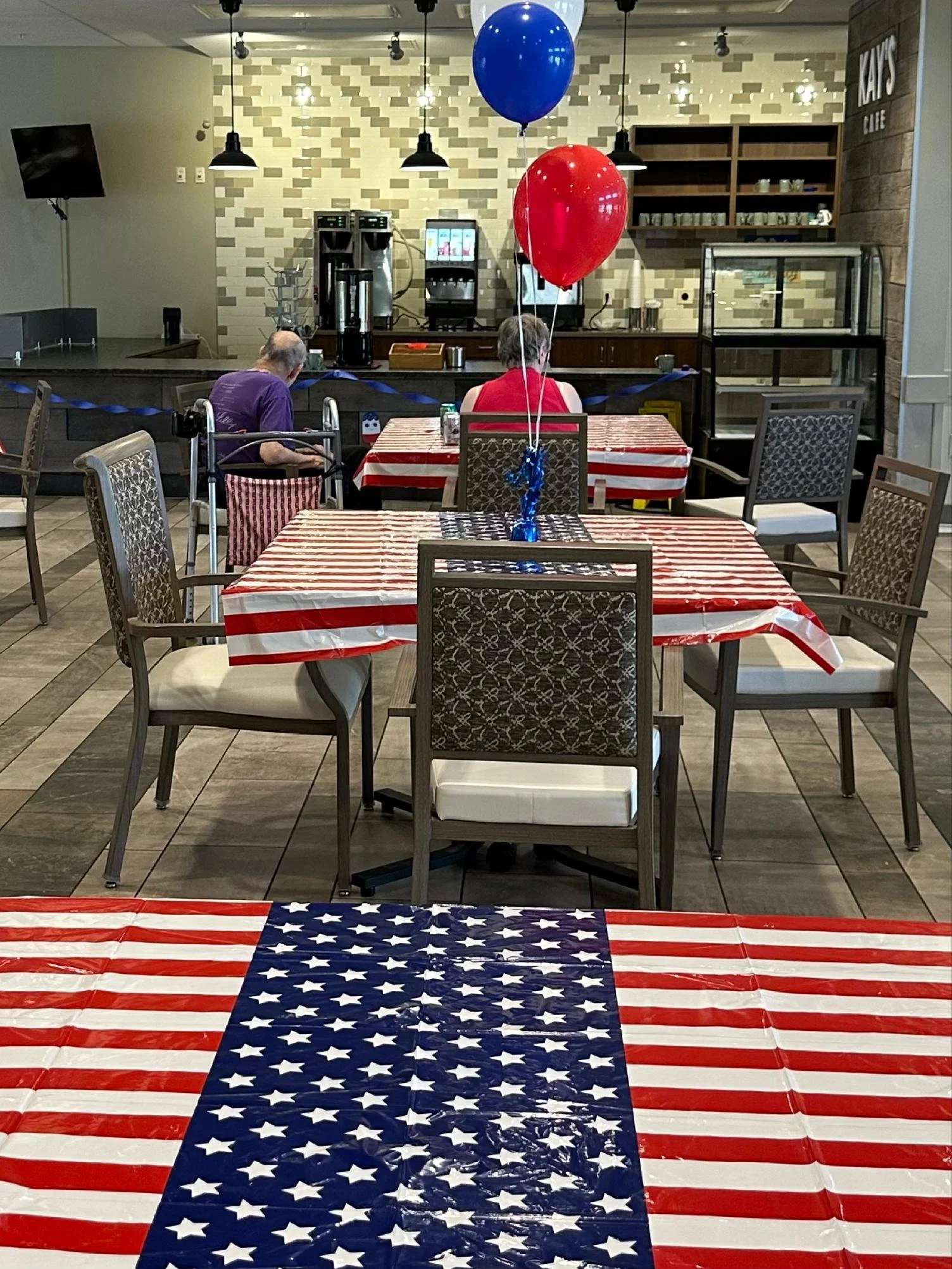 Decorated American-themed indoor space with tablecloths, balloons, and a back wall with a counter and shelves.