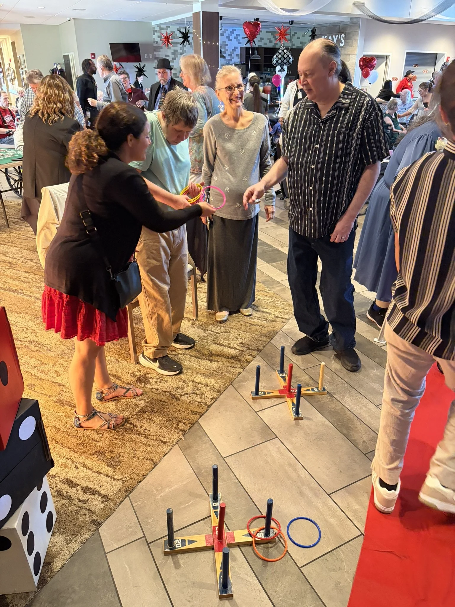 Group of people playing ring toss game at a festive event, with red and black balloons and decorations in the background.