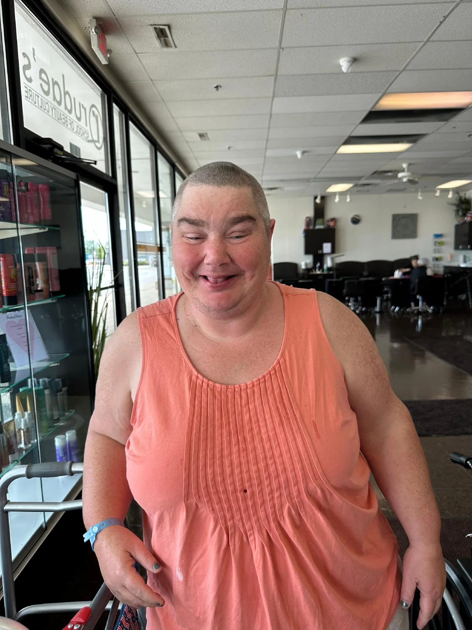 A person with short hair, wearing an orange sleeveless top, sitting in a restaurant or cafe, smiling with eyes closed.