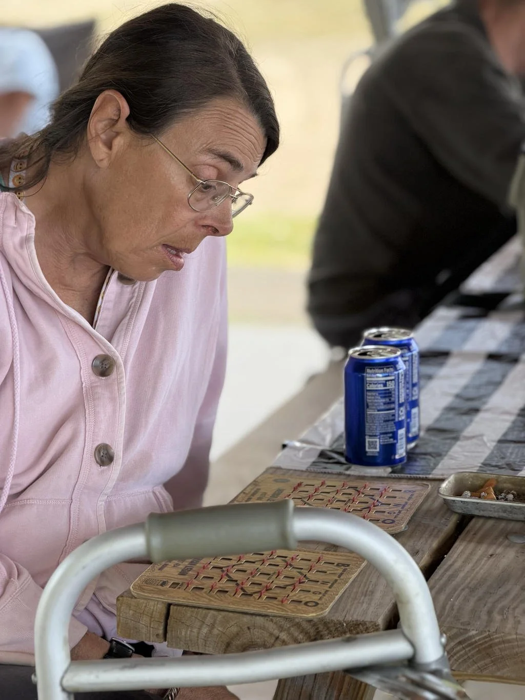 Older woman playing Bingo at a wooden table with canned drinks nearby.