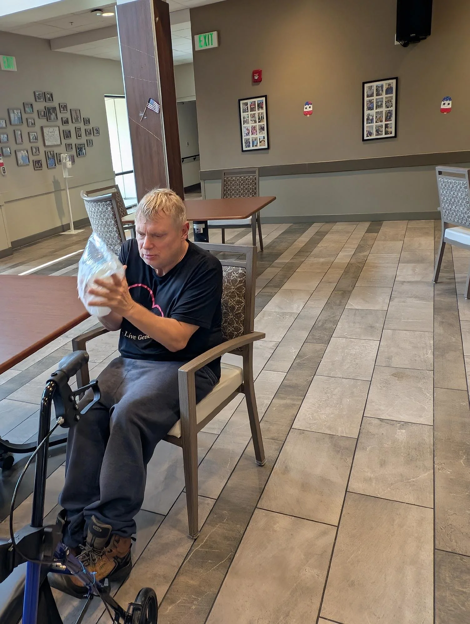 An elderly man sitting at a table, holding a paper bag, in a waiting area.