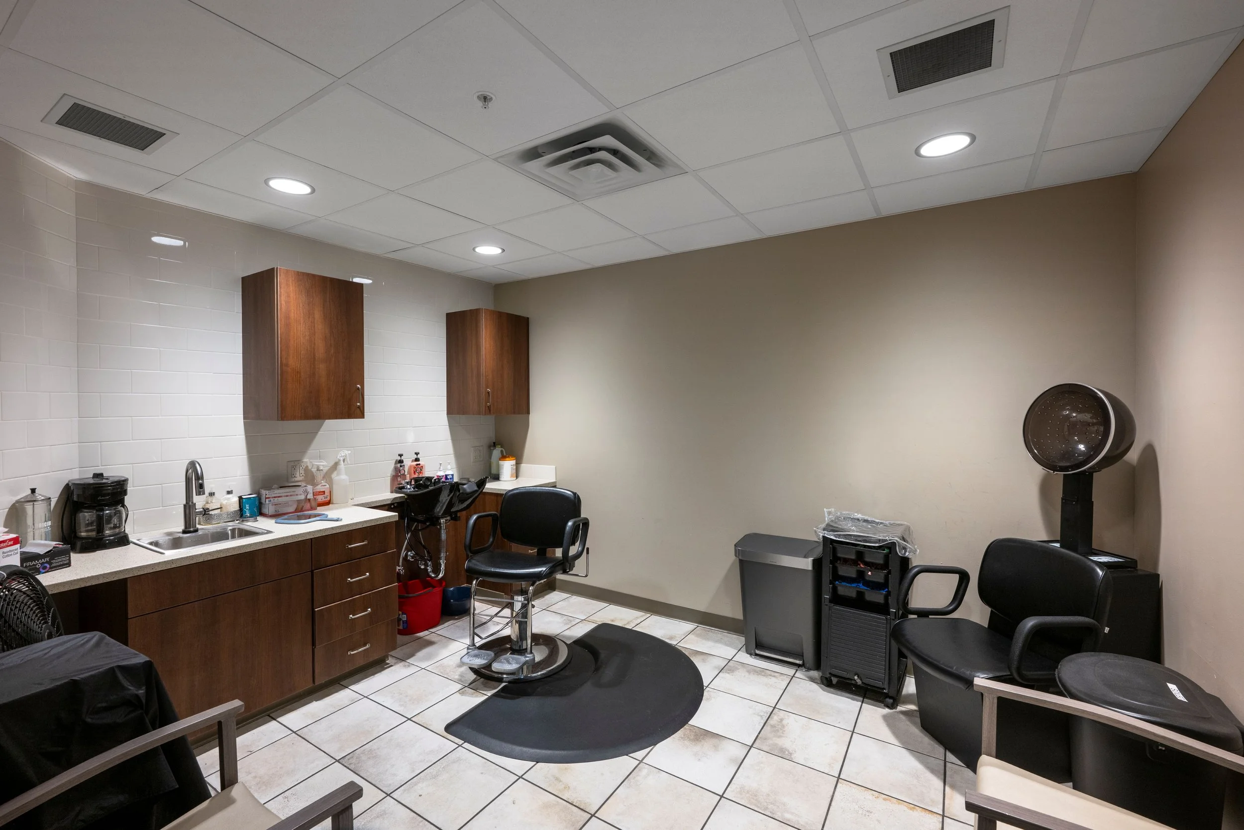 A hair salon or barber shop interior with chairs, a wash basin, cabinets, and hair styling equipment.