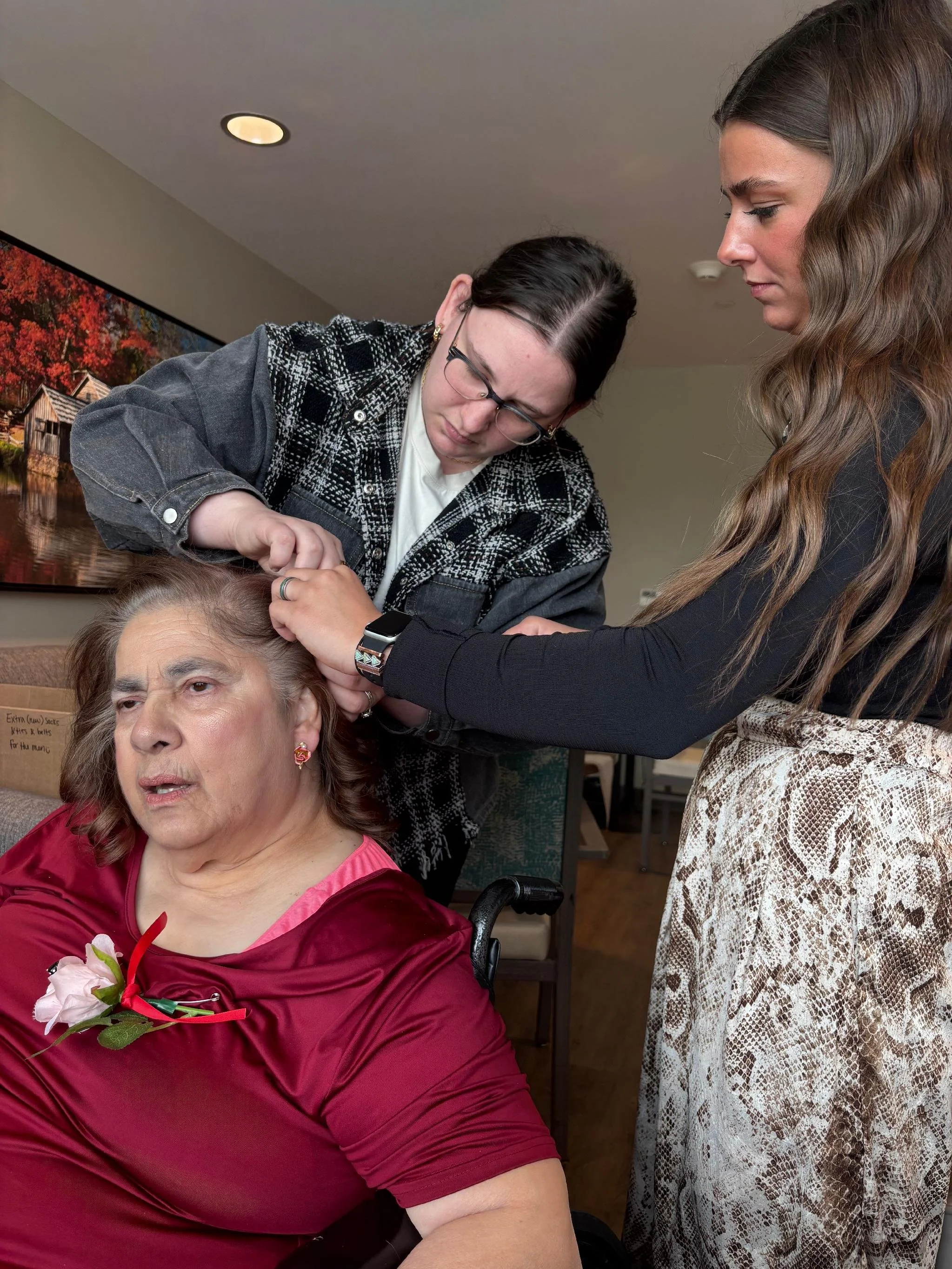 A woman receiving a haircut from a hairstylist in a salon, with a large framed landscape painting in the background.
