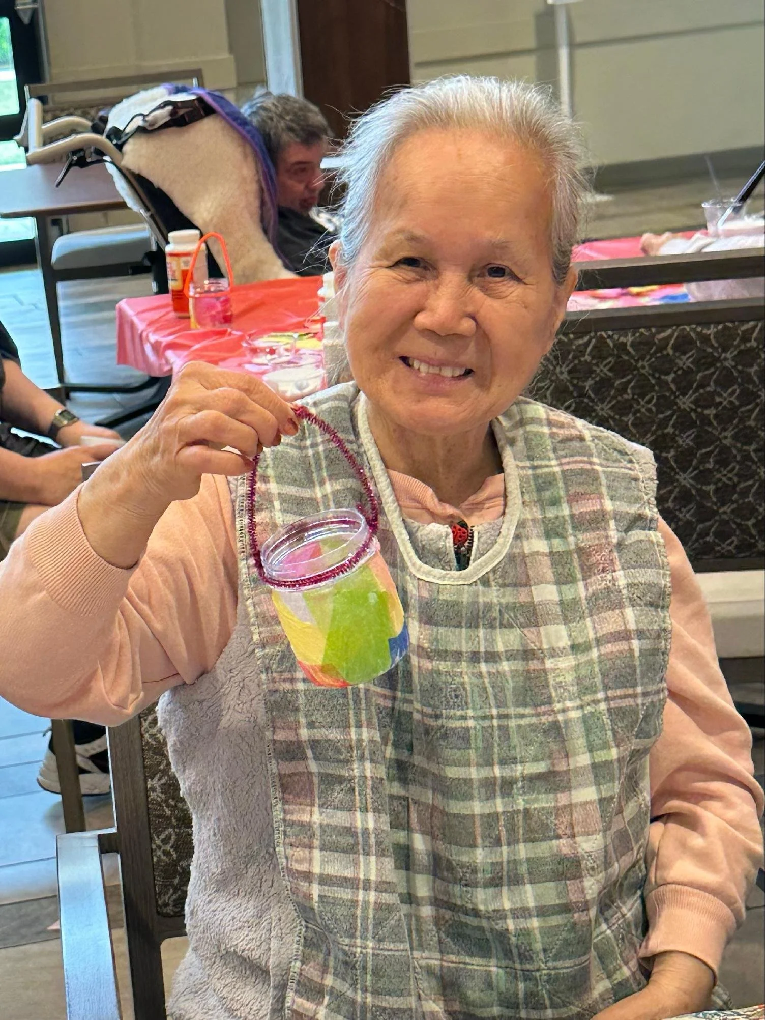 An elderly woman with gray hair, smiling and holding a small glass of colorful beverage.