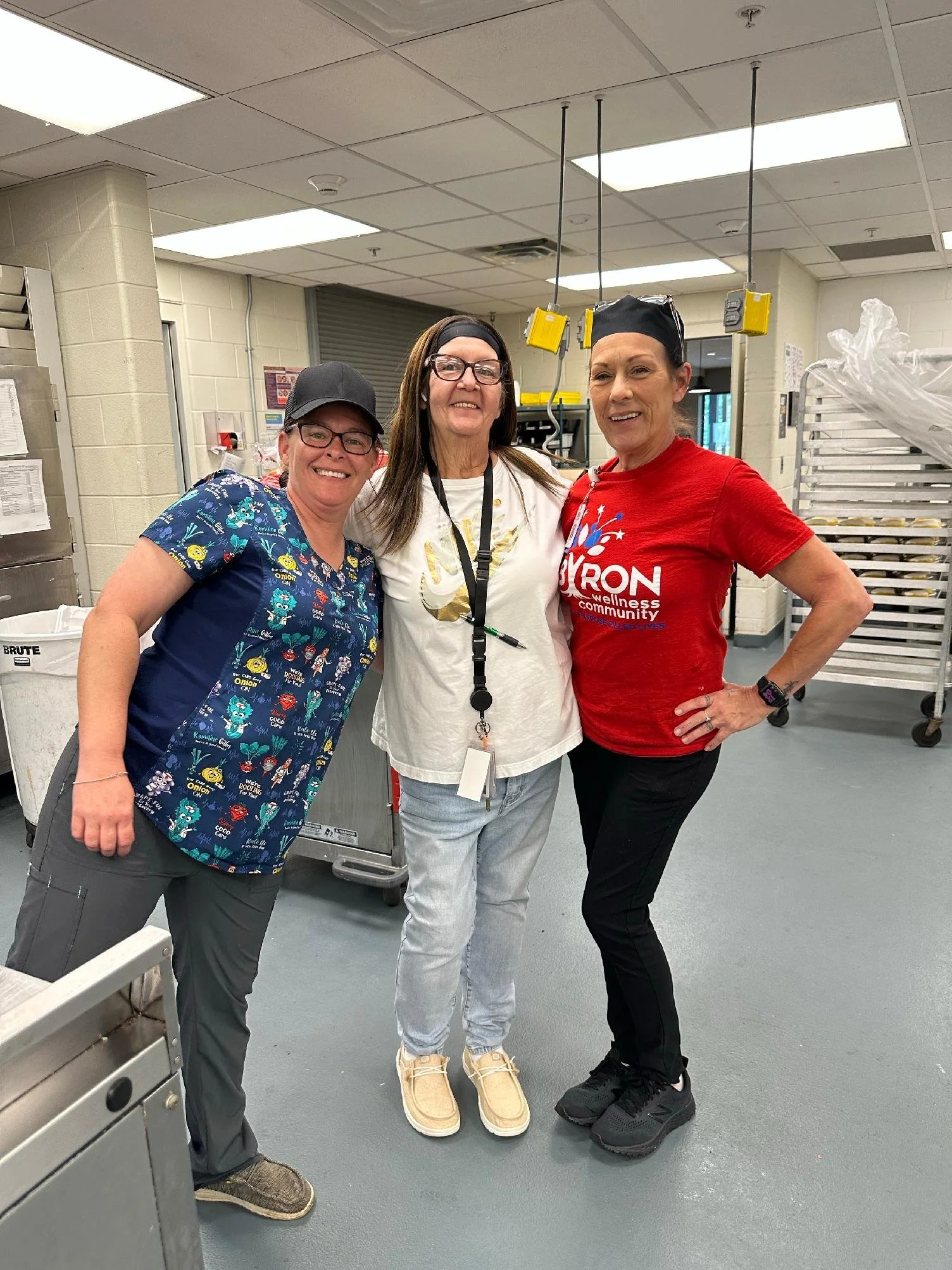 Three women standing together in a room with industrial equipment, smiling at the camera.
