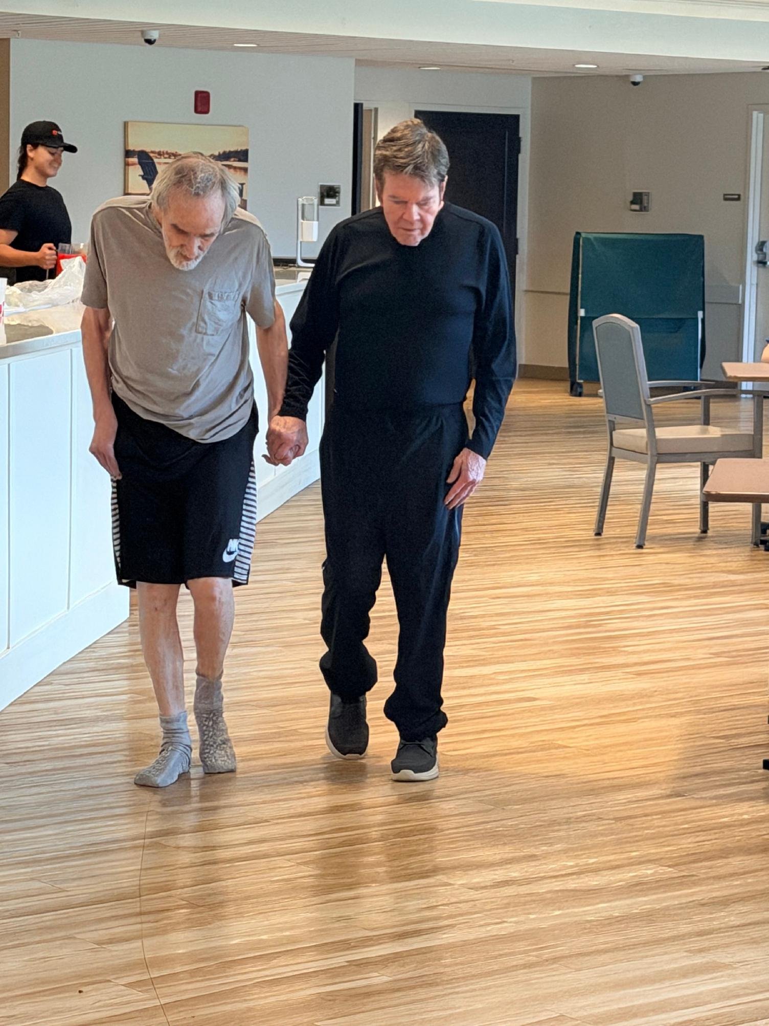 Two men and a woman walking hand-in-hand in a room with wood flooring, light-colored walls, and minimal furnishings.