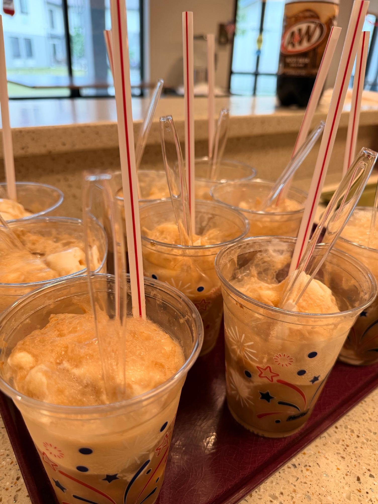 Multiple cups of orange-colored ice or frozen beverage with straws on a tray in a restaurant or cafe.