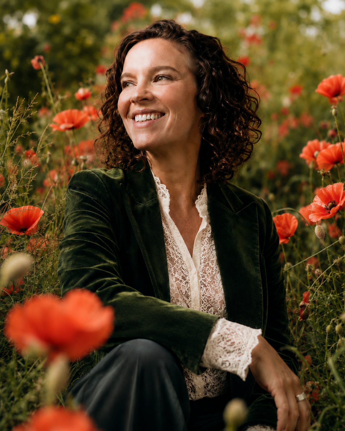 Christine Renaud smiling while sitting among red poppies in a garden.