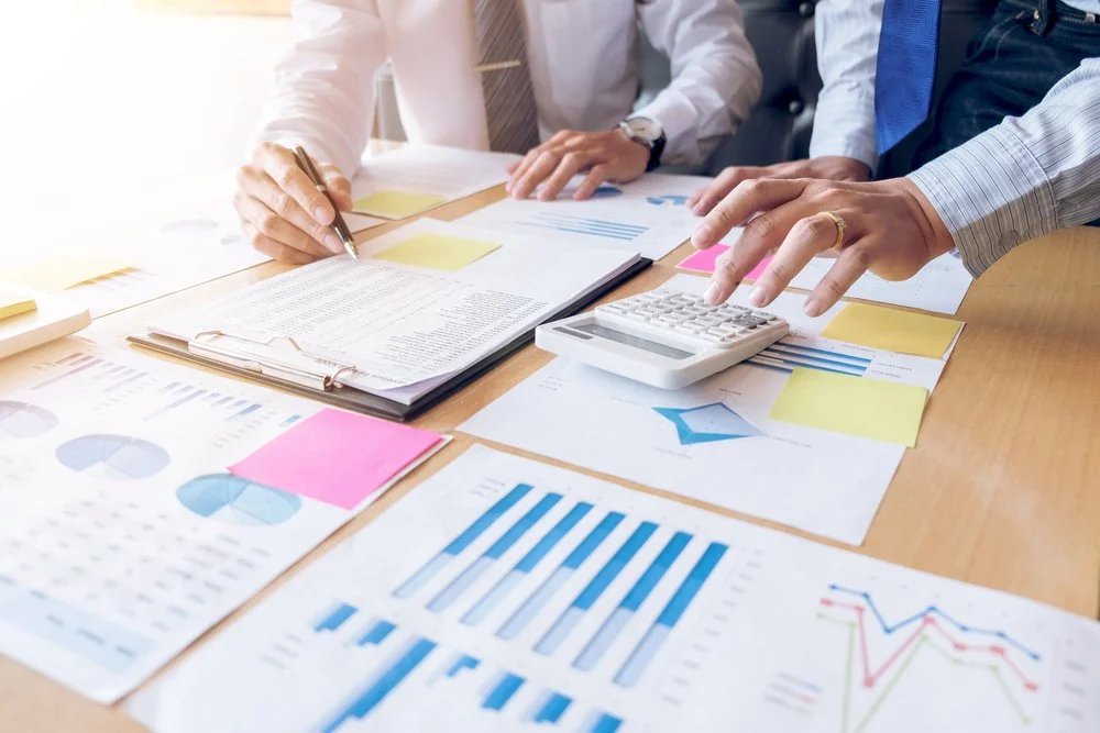 Business people reviewing financial charts and documents on a desk with a calculator.