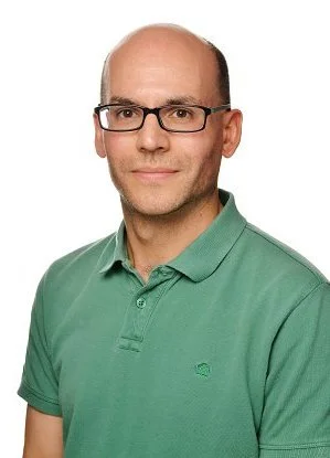 Portrait of a man wearing glasses and a green polo shirt, smiling slightly.