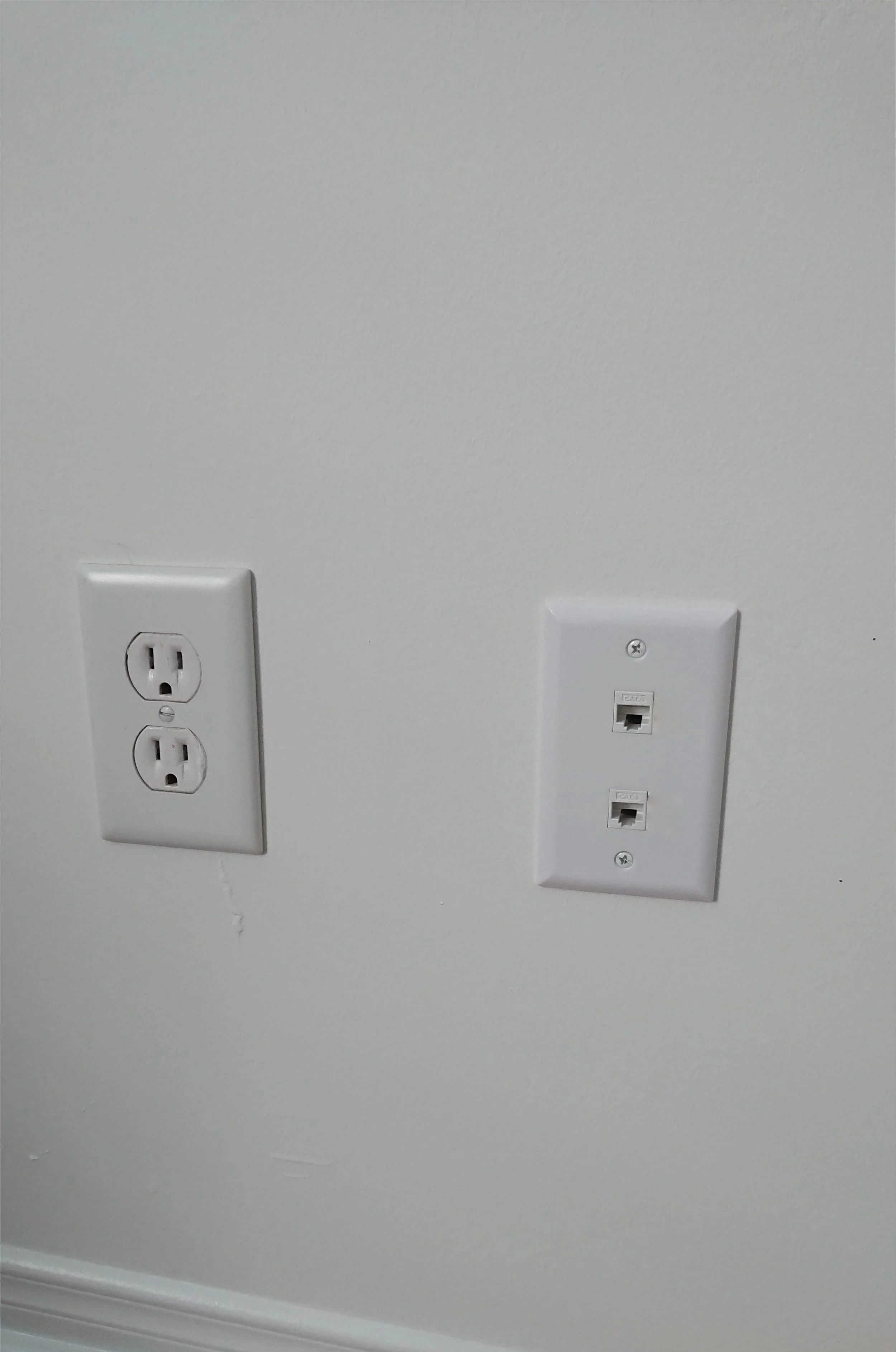 Photo of a wall with a standard two-outlet electrical socket on the left and a wall plate with two Ethernet jacks on the right.