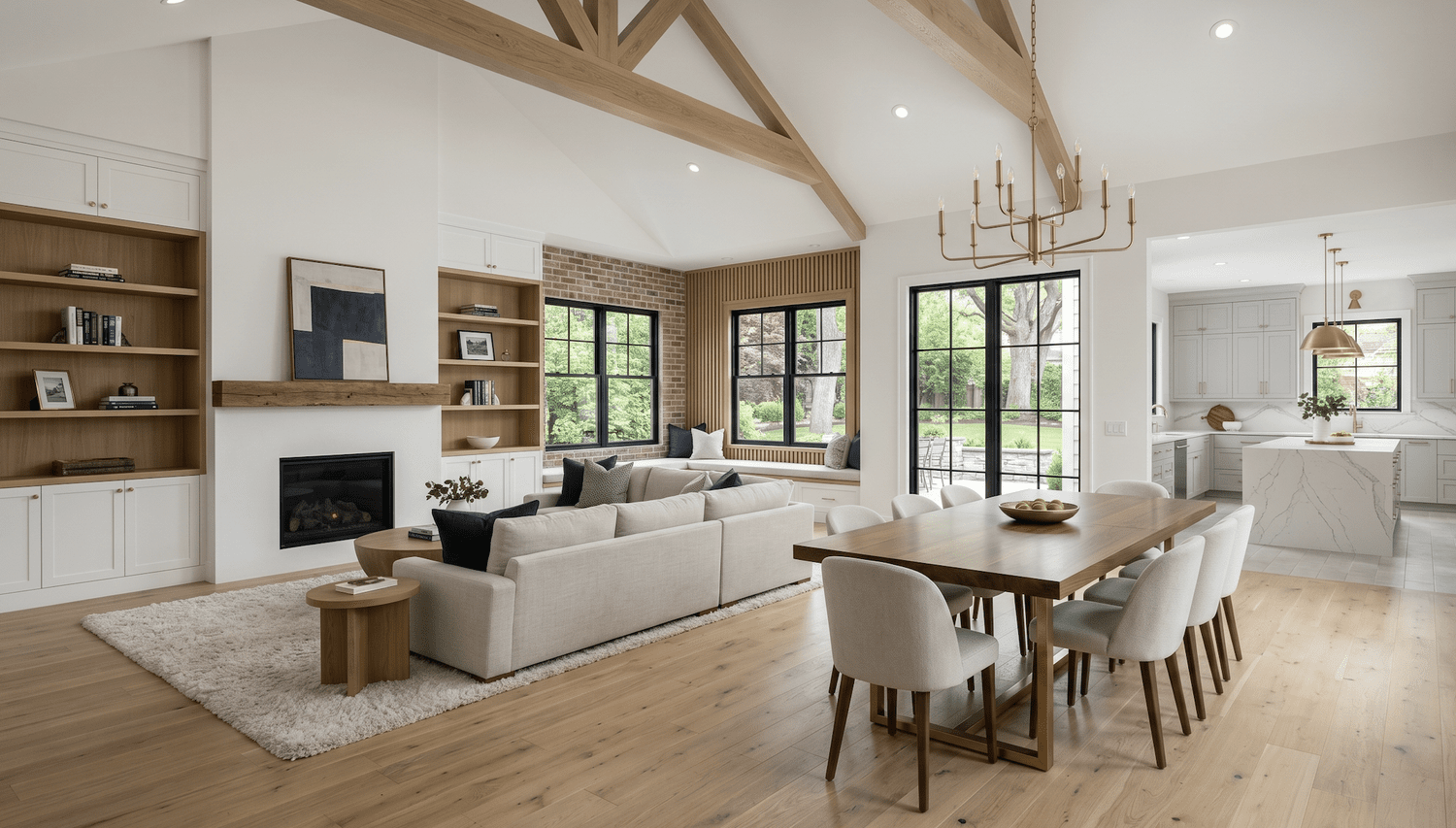 Modern open-concept living room, dining area, and white kitchen with exposed wood beams, fireplace, large windows, and marble island