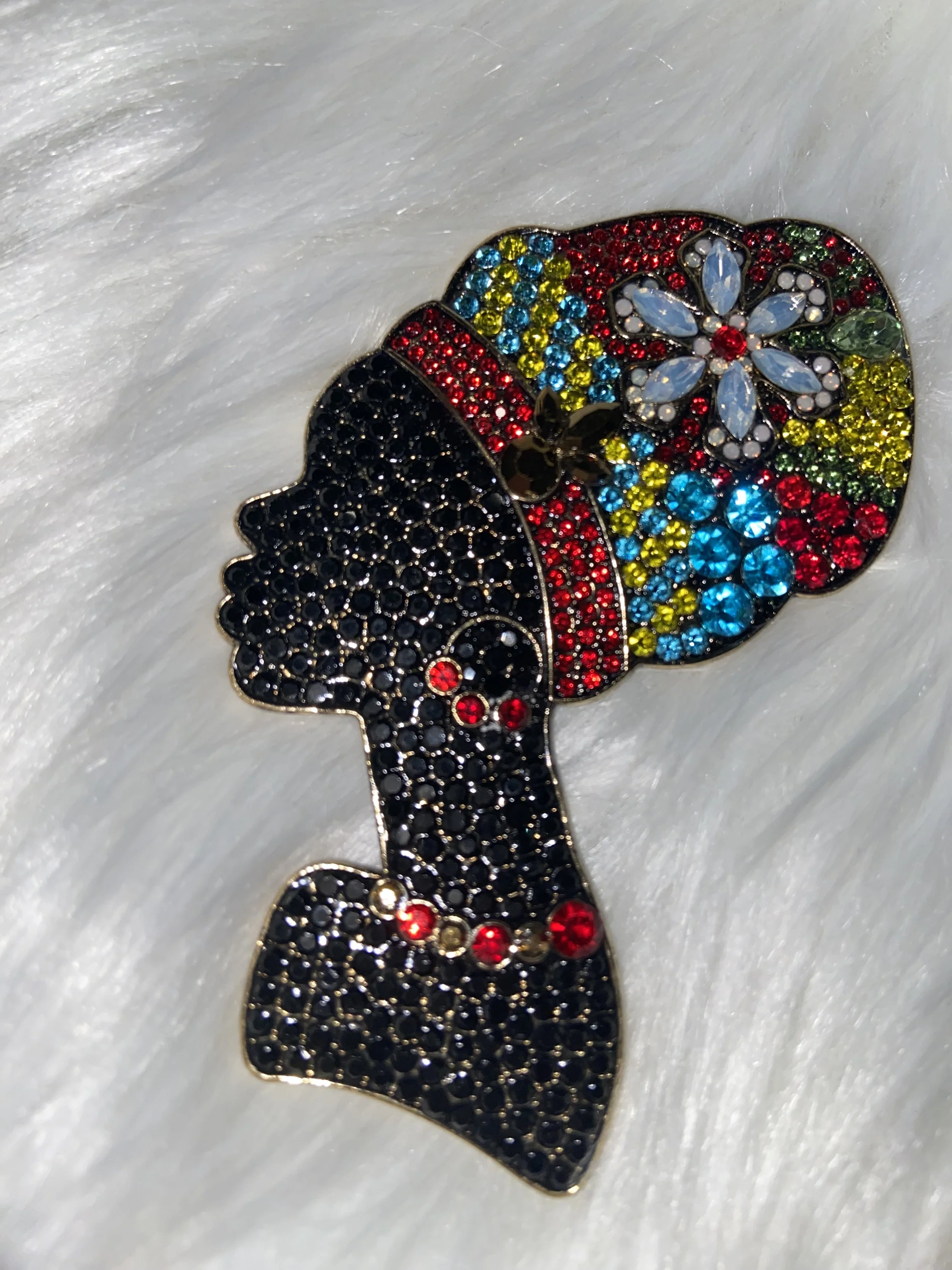 Colorful rhinestone brooch in the shape of a woman with a floral headpiece, placed on a white, fuzzy fabric background.