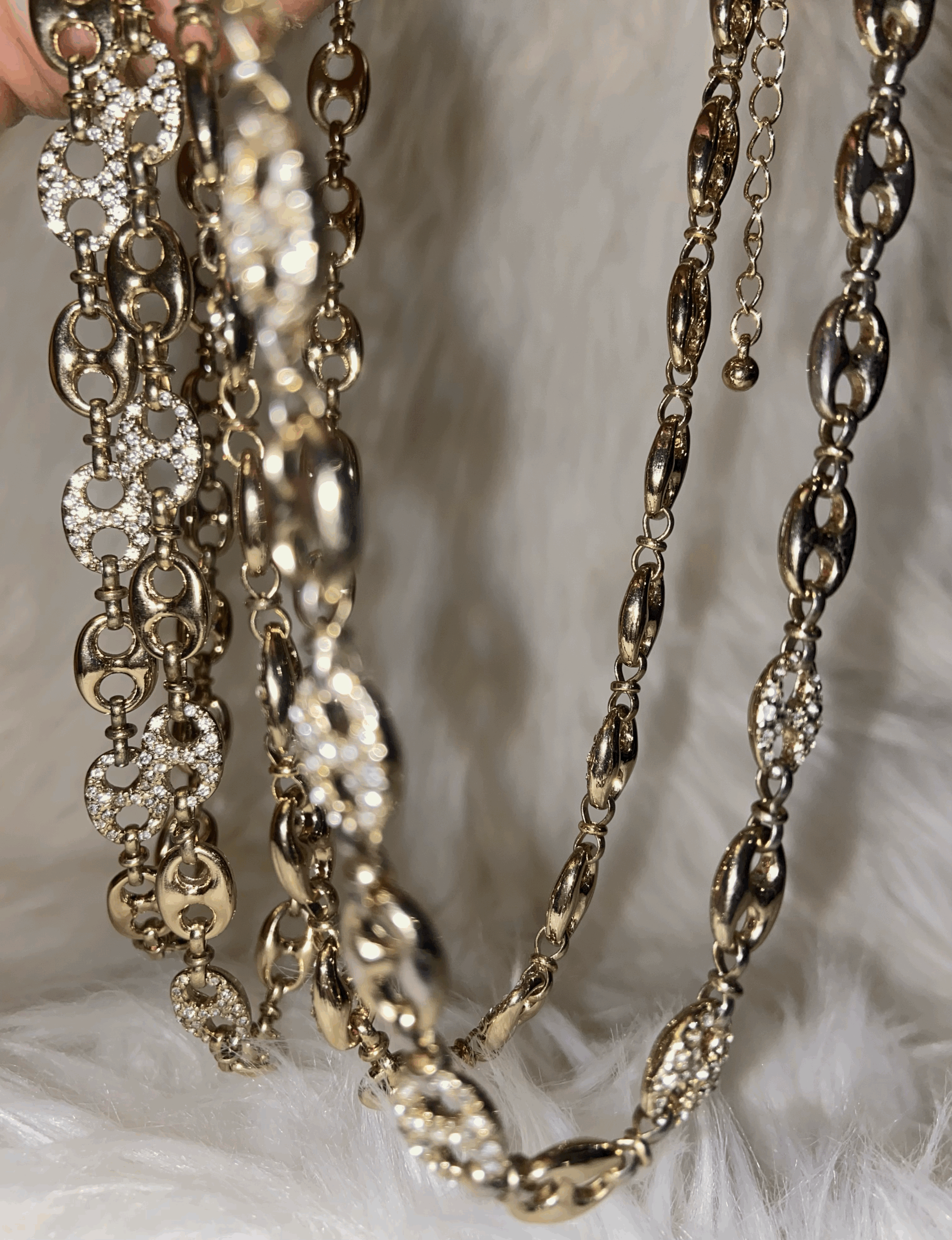 LOF inspired cuban link chains with circular and oval links, some adorned with small, sparkling rhinestones, hanging against a soft white, furry surface.