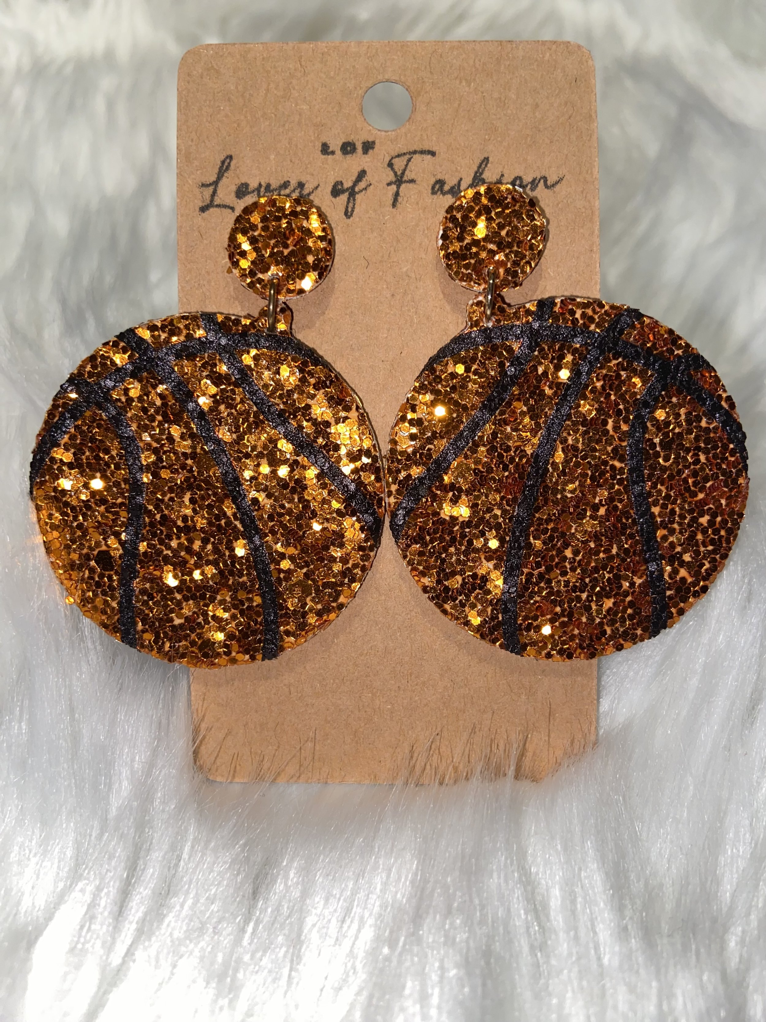 Gold glittery basketball-shaped earrings on a brown paper card, with the brand name 'Lover of Fashion' written on it.