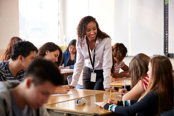 Female teacher standing and interacting with students in a classroom.